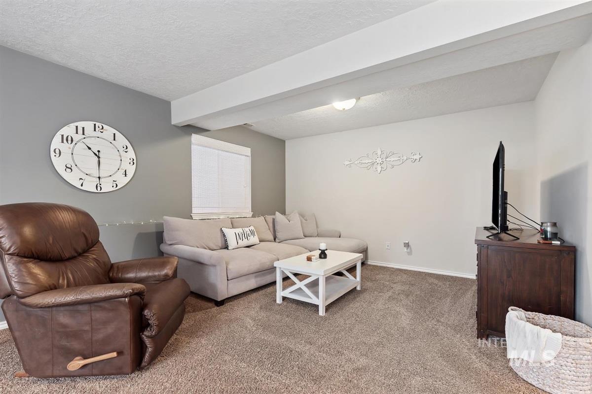 Carpeted living area featuring a textured ceiling and beamed ceiling