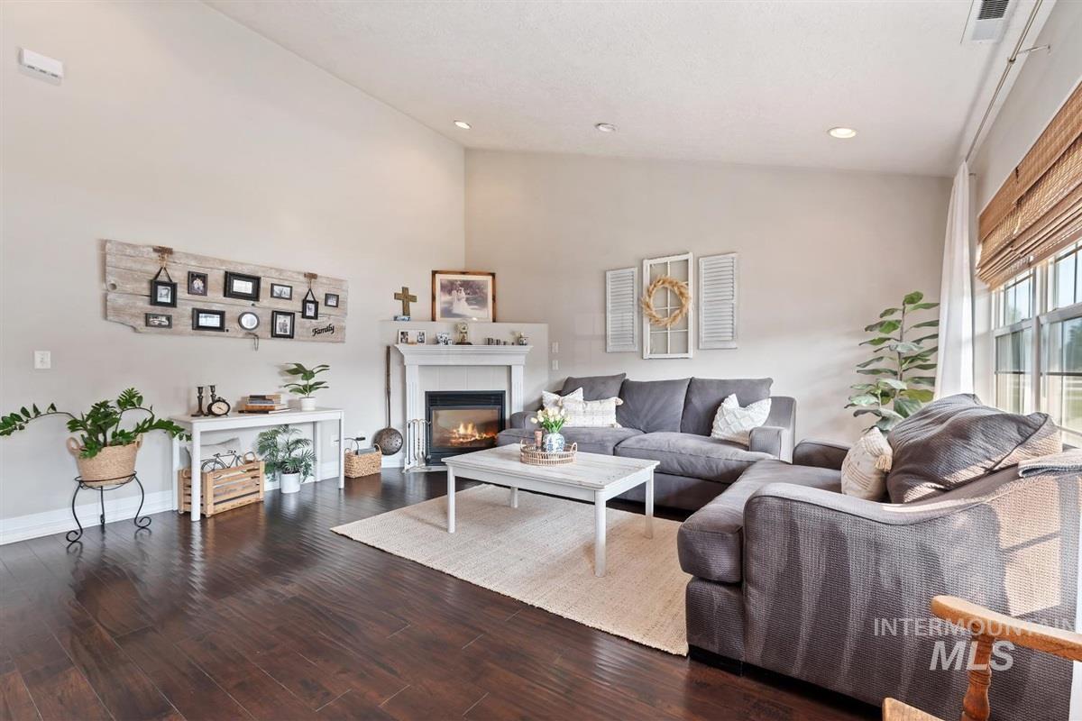 Living area with a glass covered fireplace, wood finished floors, high vaulted ceiling, and recessed lighting