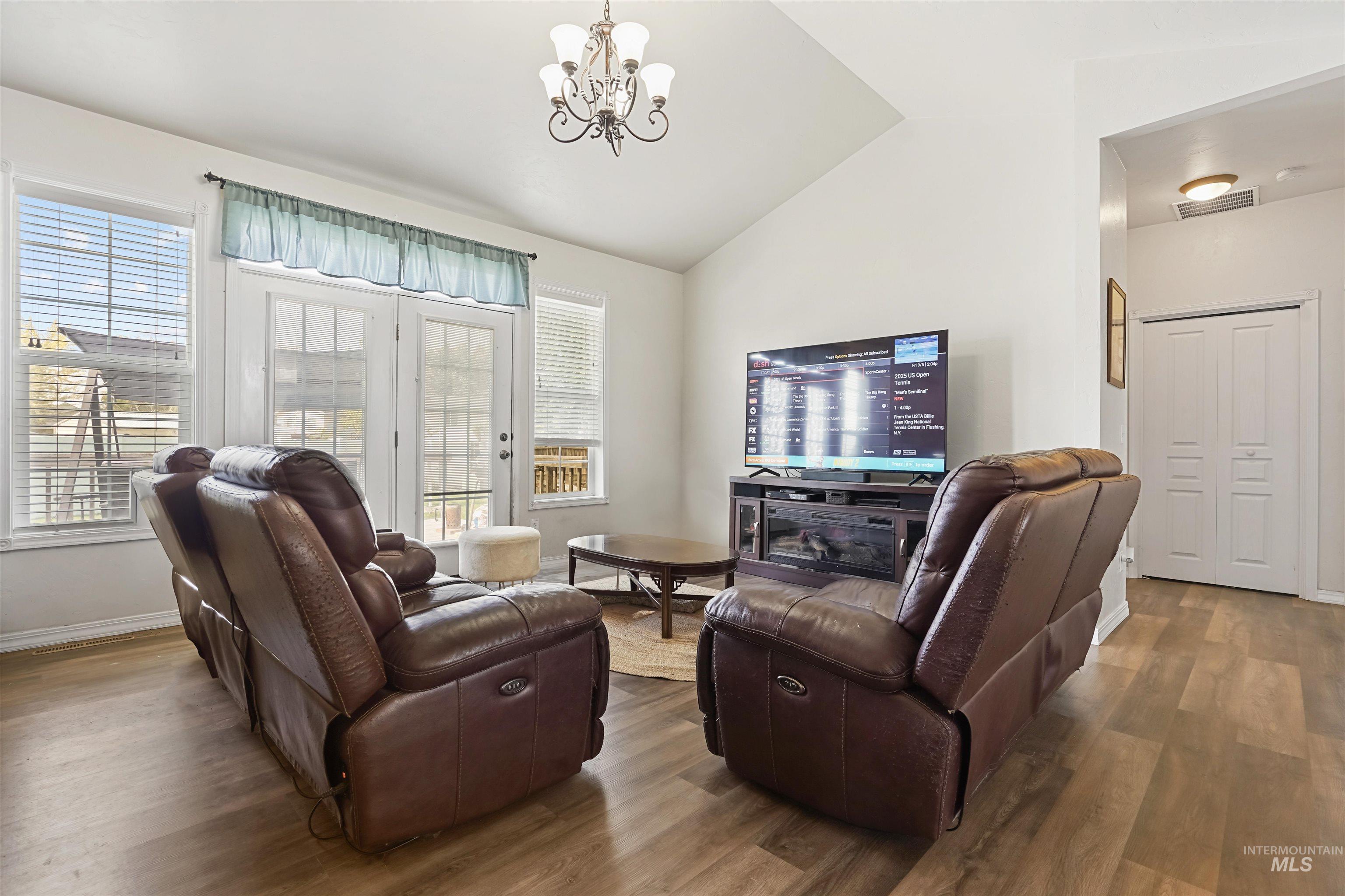 Living room with lofted ceiling, wood finished floors, healthy amount of natural light, and a chandelier