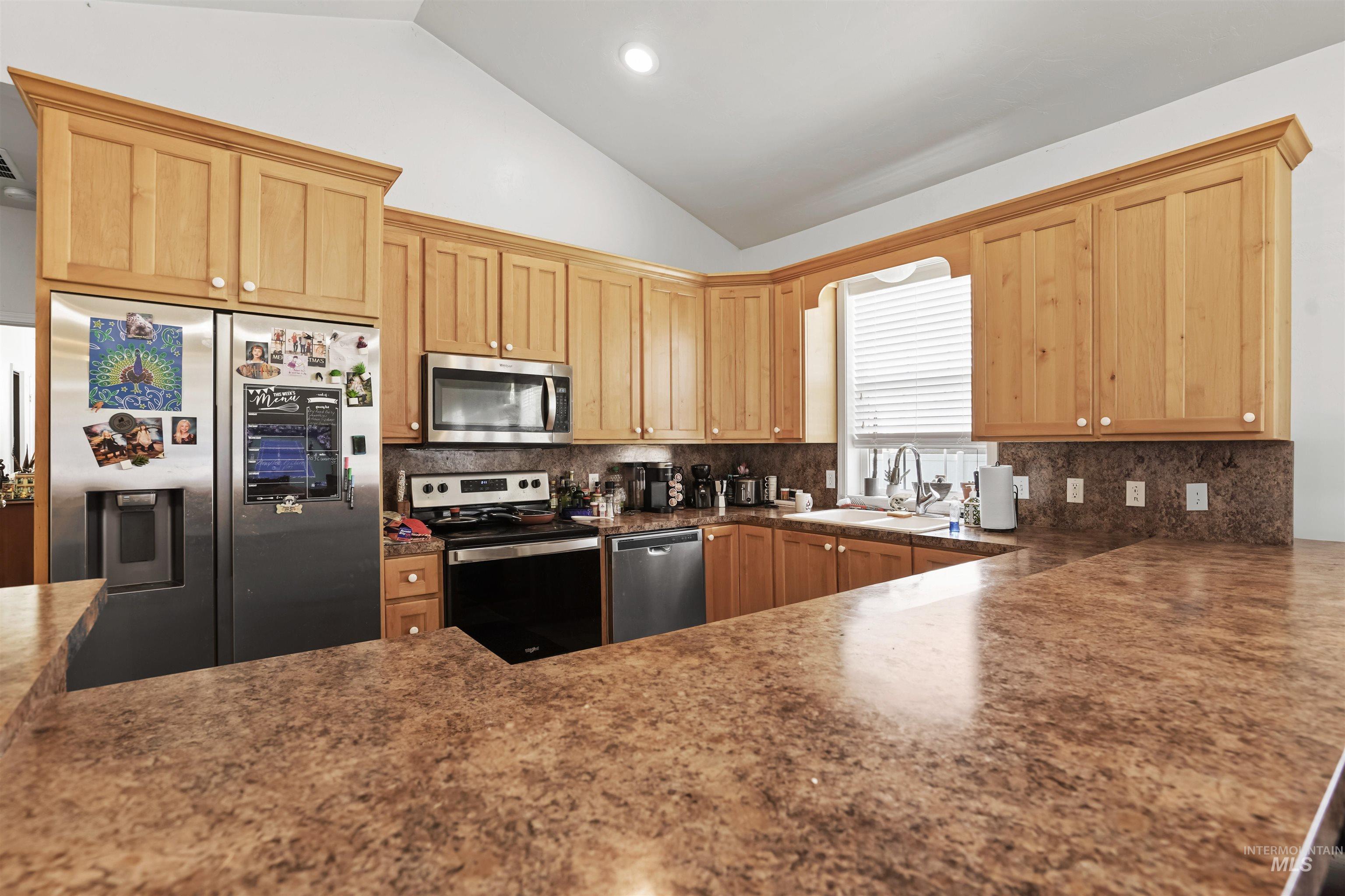 Kitchen featuring appliances with stainless steel finishes, tasteful backsplash, light brown cabinets, lofted ceiling, and recessed lighting