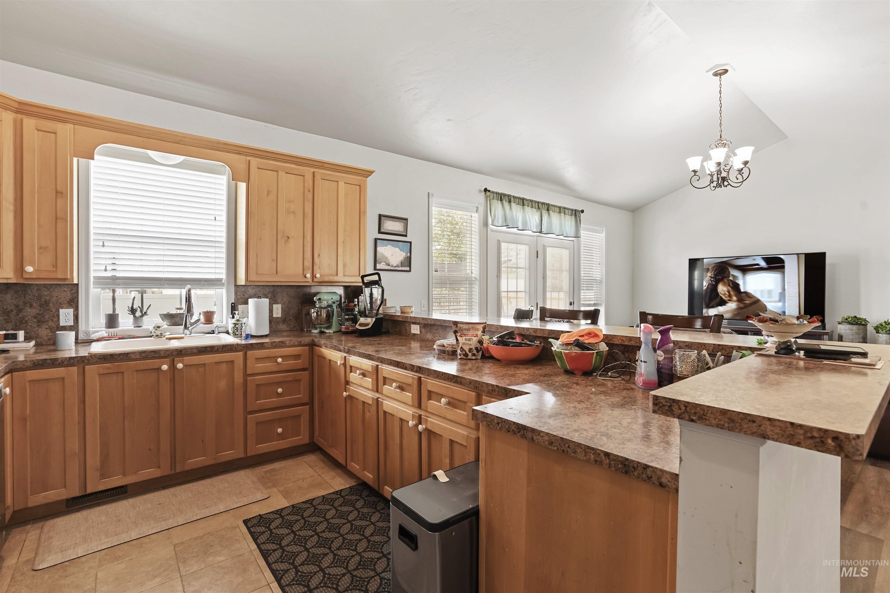 Kitchen featuring dark countertops, a peninsula, light tile patterned floors, decorative backsplash, and lofted ceiling