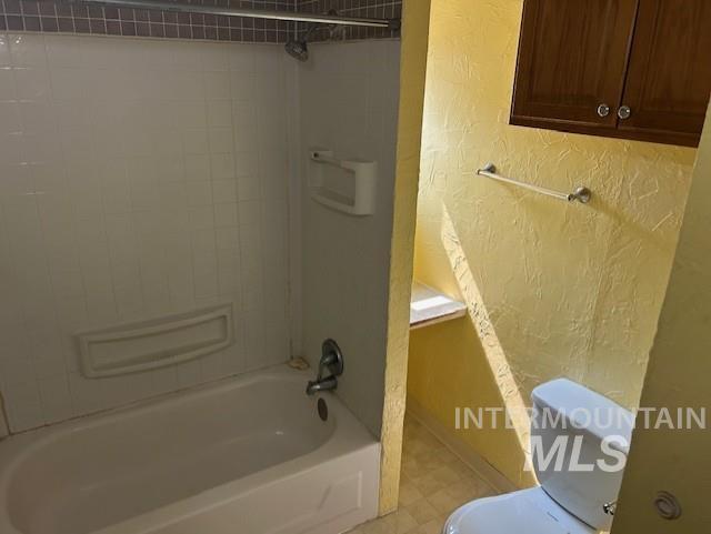 Bathroom with a textured wall and bathing tub / shower combination