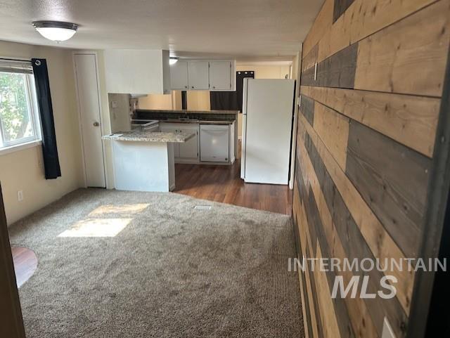 Kitchen with white appliances, dark colored carpet, white cabinets, a peninsula, and wooden walls