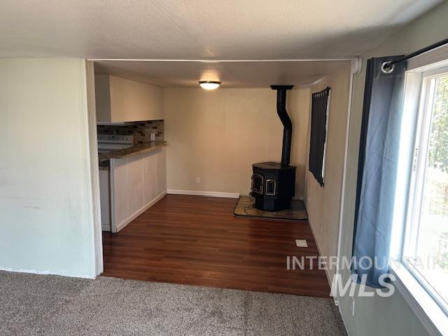 Unfurnished living room with a wood stove, dark colored carpet, and dark wood-style flooring