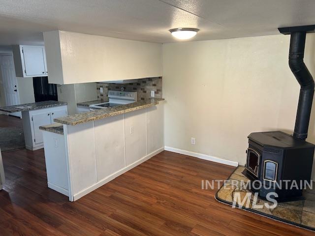 Kitchen featuring a wood stove, white cabinetry, white electric range oven, and a peninsula