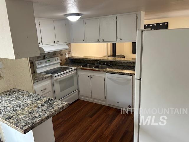 Kitchen with white appliances, white cabinets, dark wood finished floors, a peninsula, and decorative backsplash