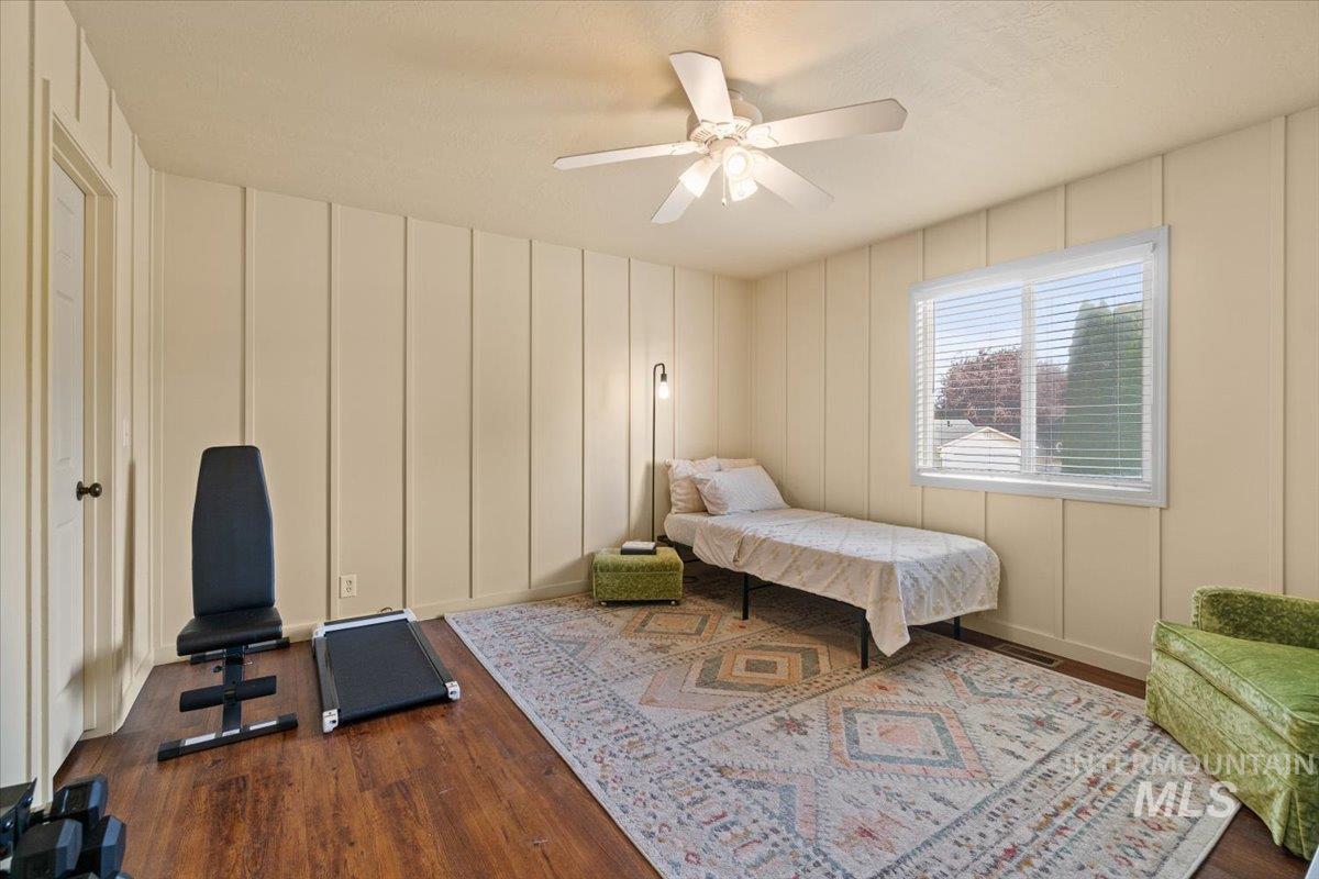 Bedroom with a decorative wall, dark wood-style floors, and ceiling fan