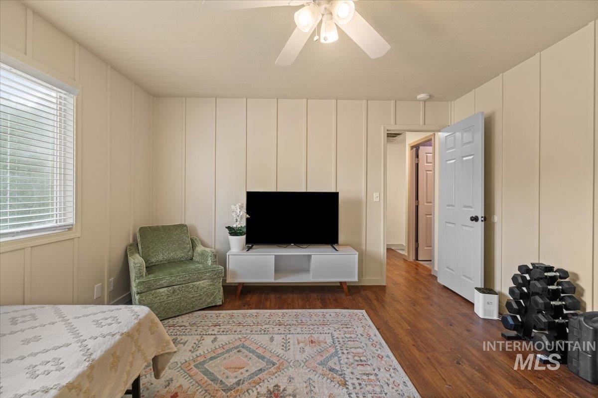 Bedroom with a decorative wall, dark wood finished floors, and a ceiling fan