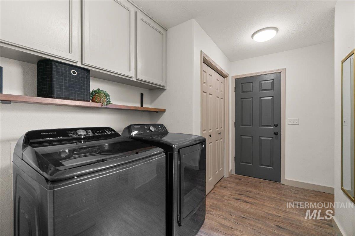 Laundry area featuring dark wood-style flooring, washing machine and clothes dryer, and cabinet space