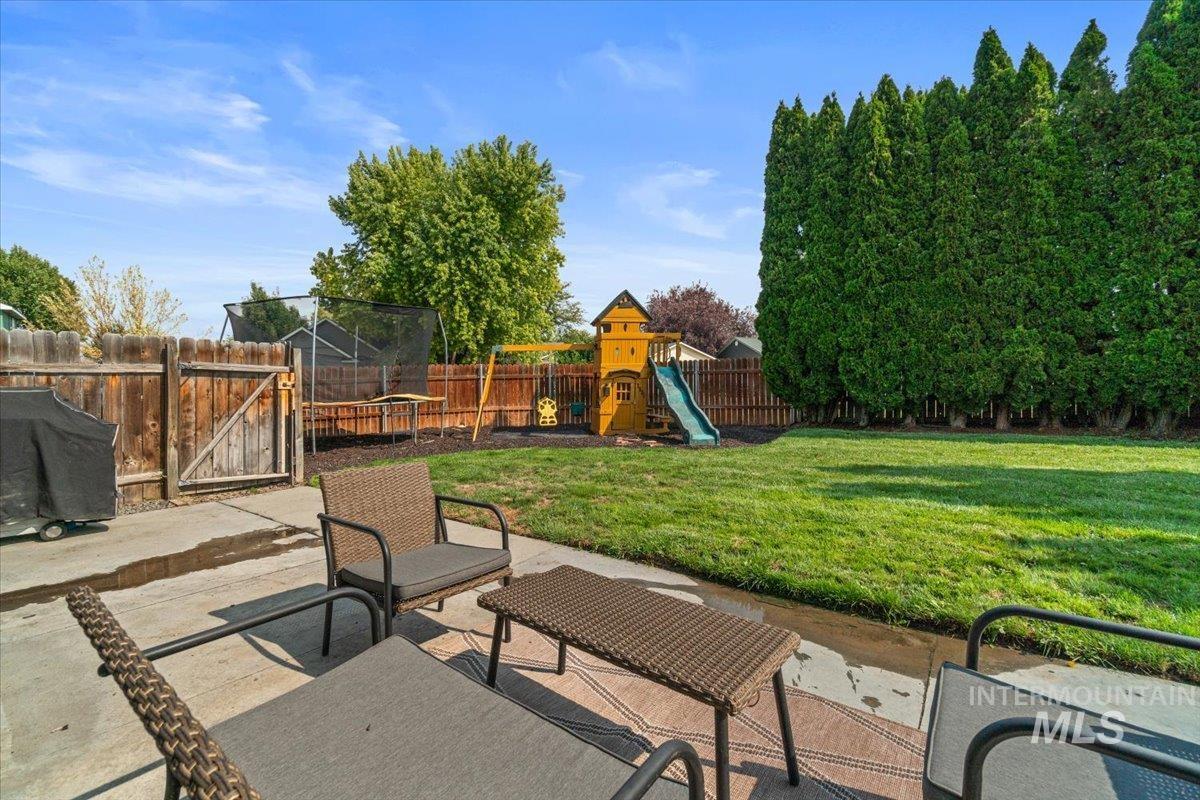 Fenced backyard featuring a patio, a playground, and a trampoline