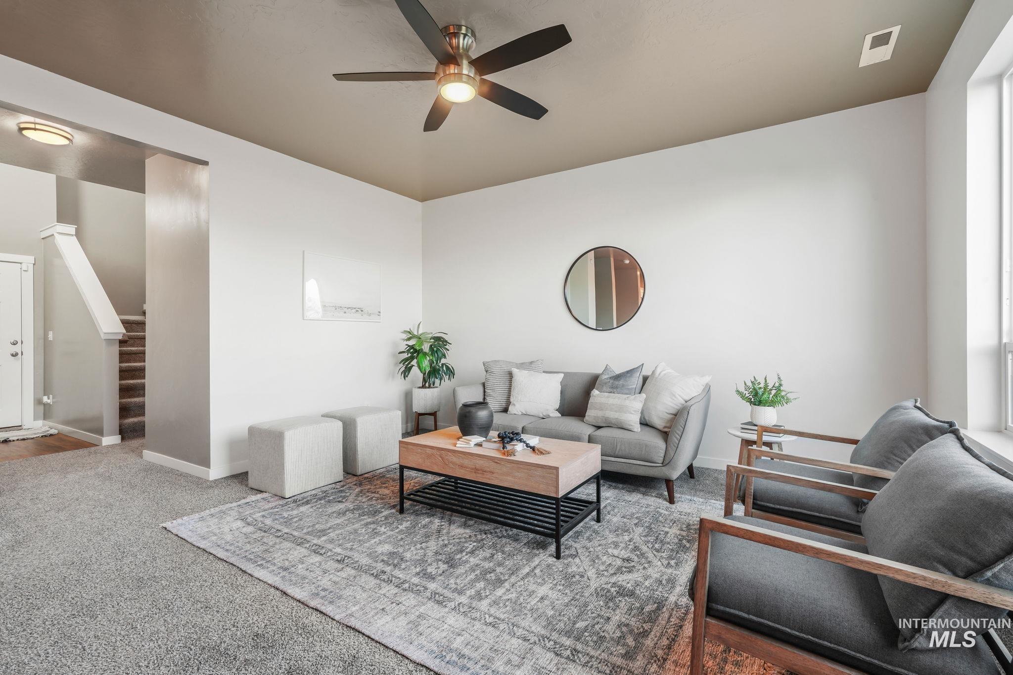 Carpeted living room featuring ceiling fan and stairway