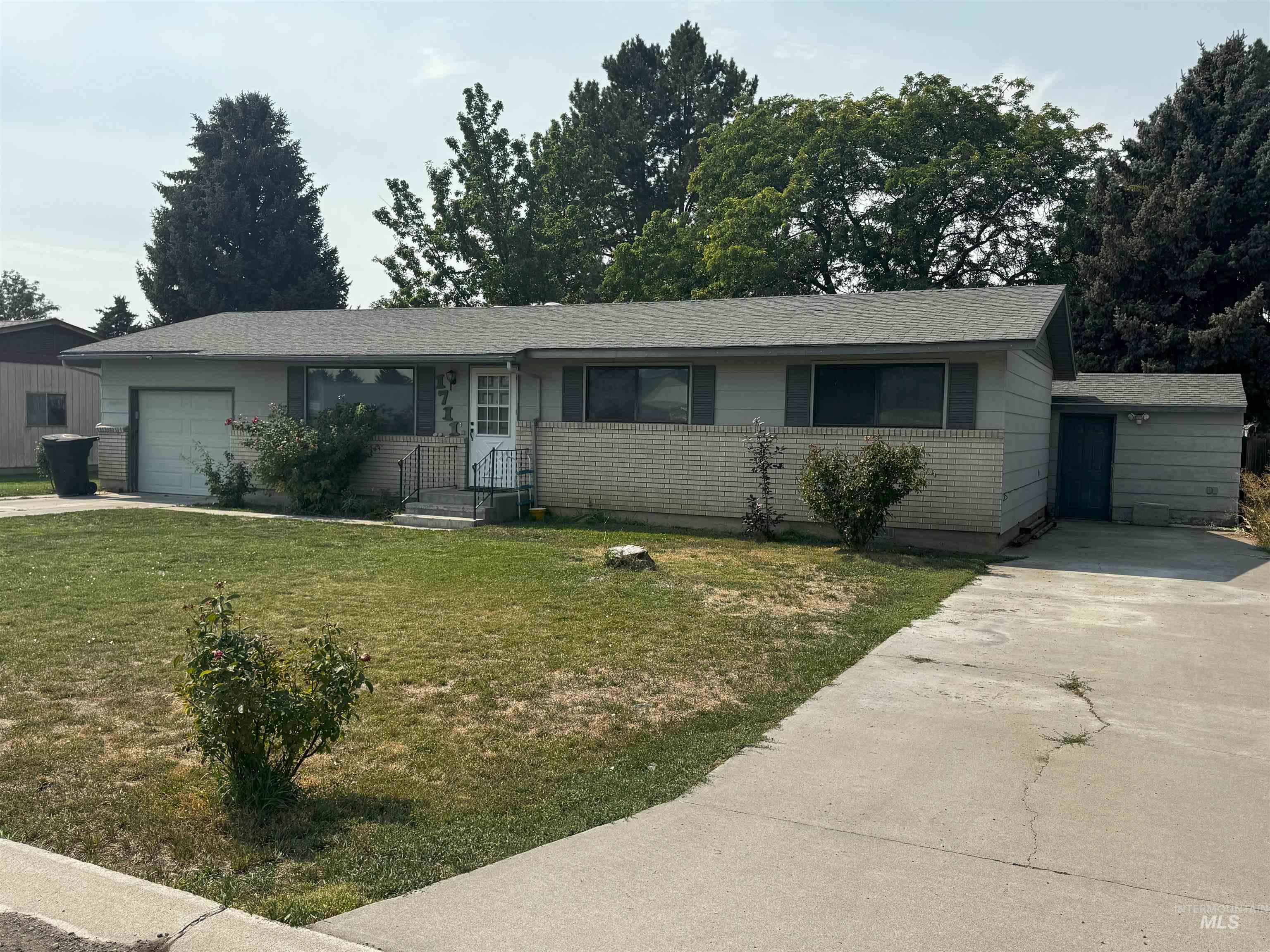 Ranch-style house featuring concrete driveway, a front yard, a garage, and a shingled roof
