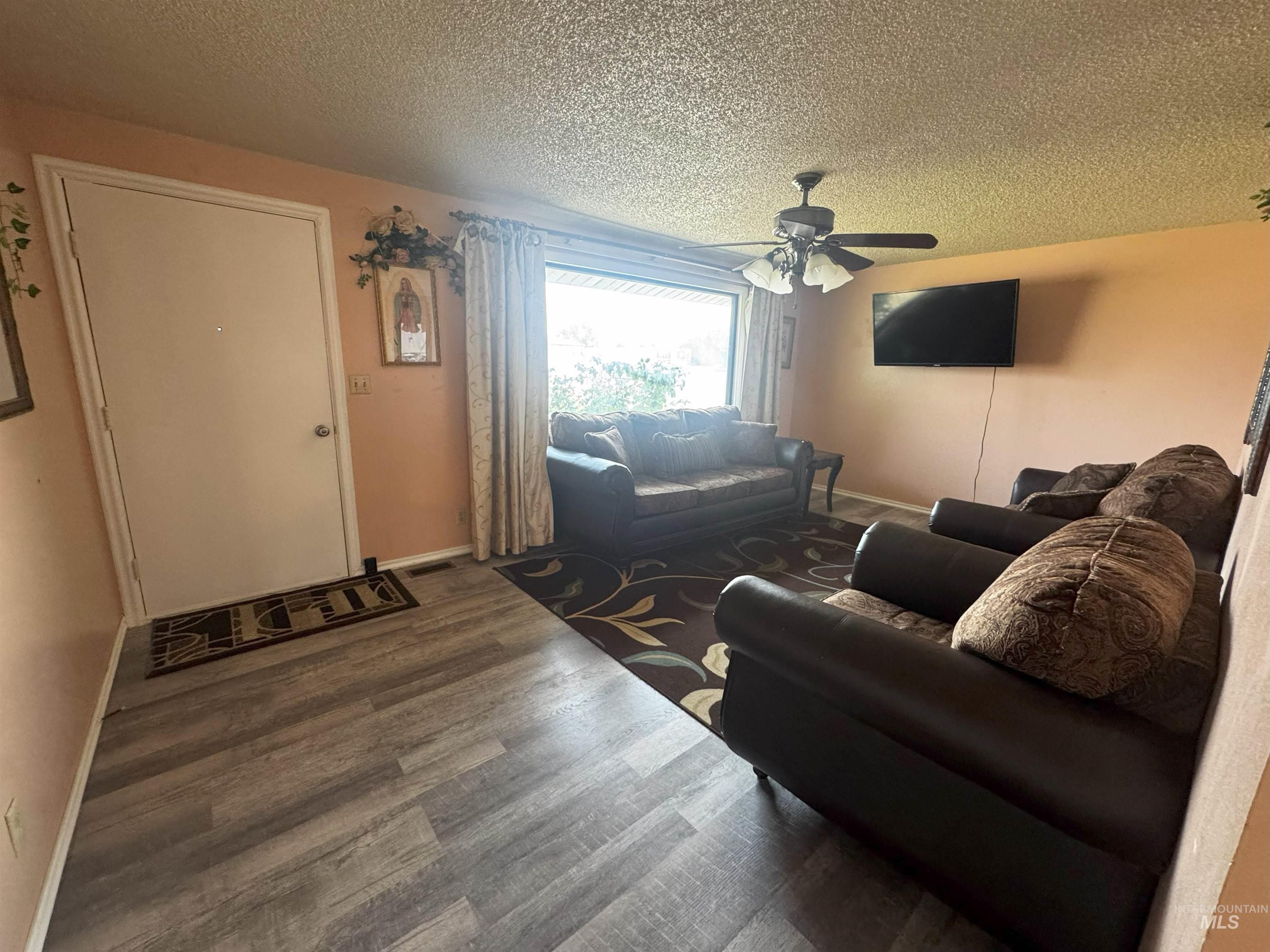 Living area with a textured ceiling, wood finished floors, and a ceiling fan