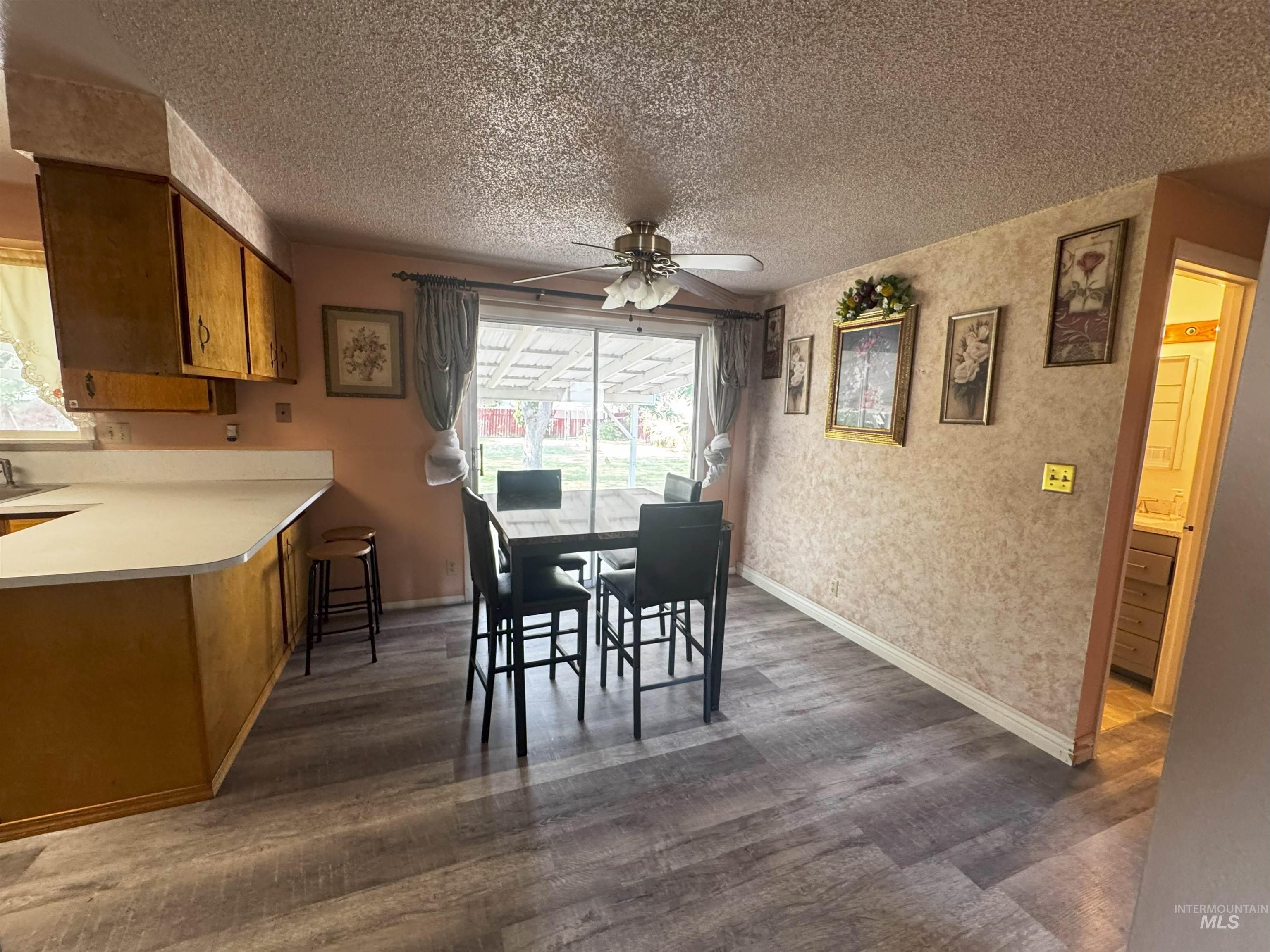 Dining area with dark wood-style flooring, a textured ceiling, wallpapered walls, and ceiling fan