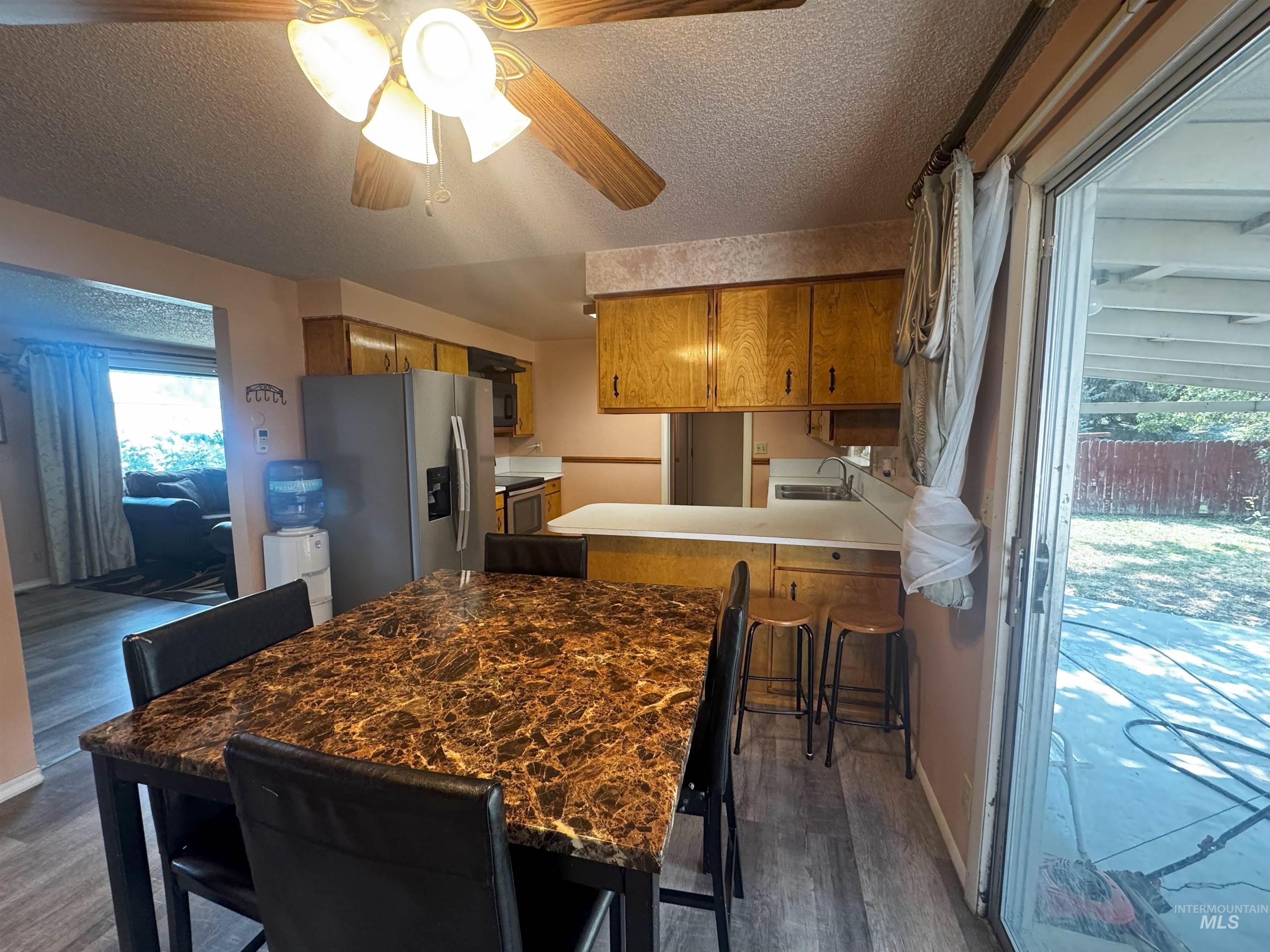 Kitchen with a peninsula, brown cabinetry, a textured ceiling, dark wood-style floors, and stainless steel appliances
