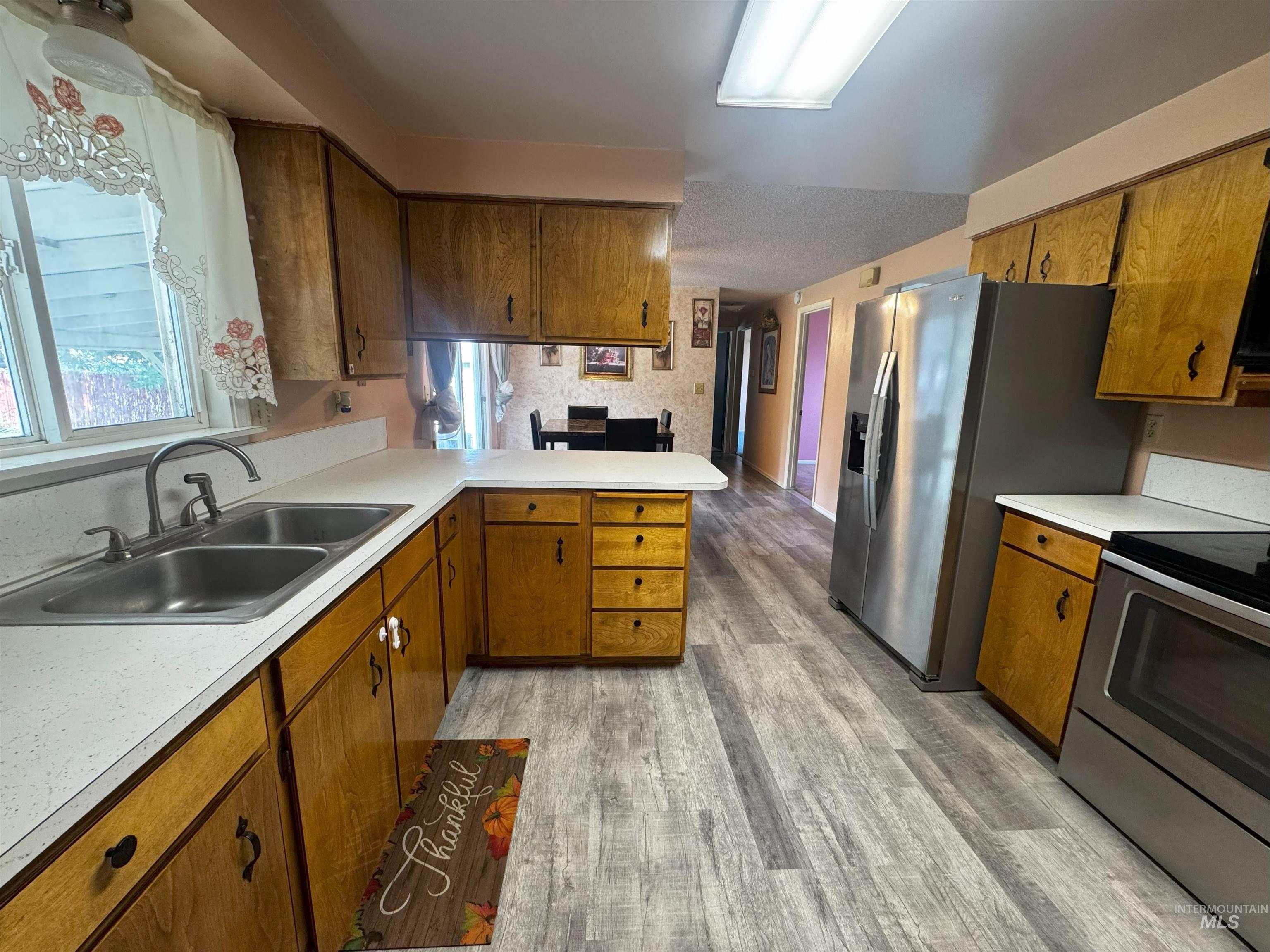 Kitchen featuring brown cabinets, stainless steel appliances, light countertops, a peninsula, and light wood-style floors