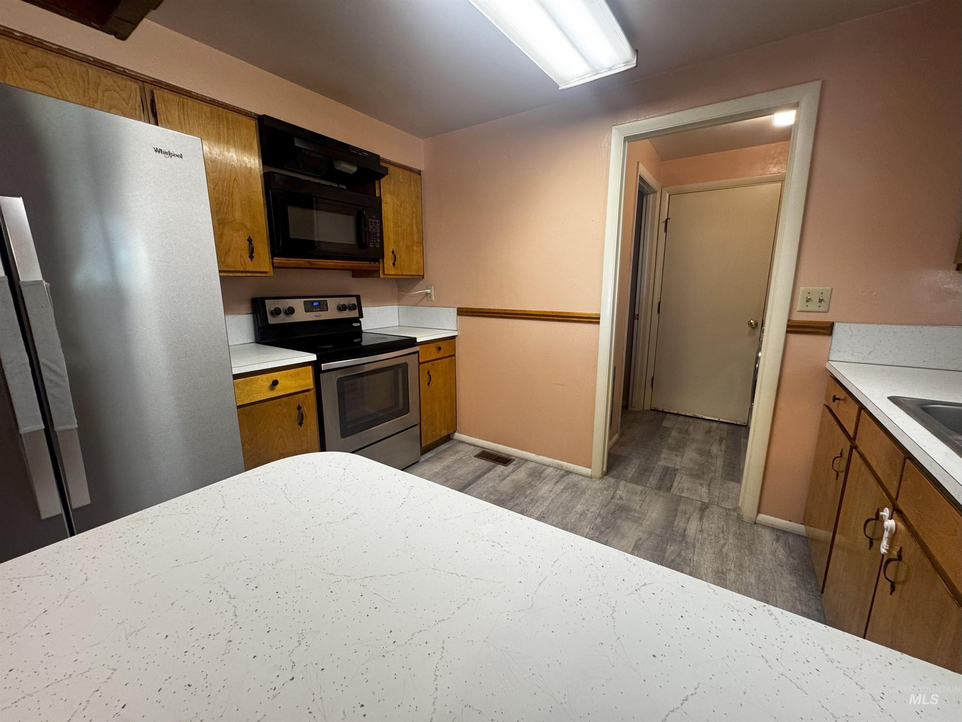 Kitchen featuring brown cabinets, appliances with stainless steel finishes, light countertops, and light wood-type flooring