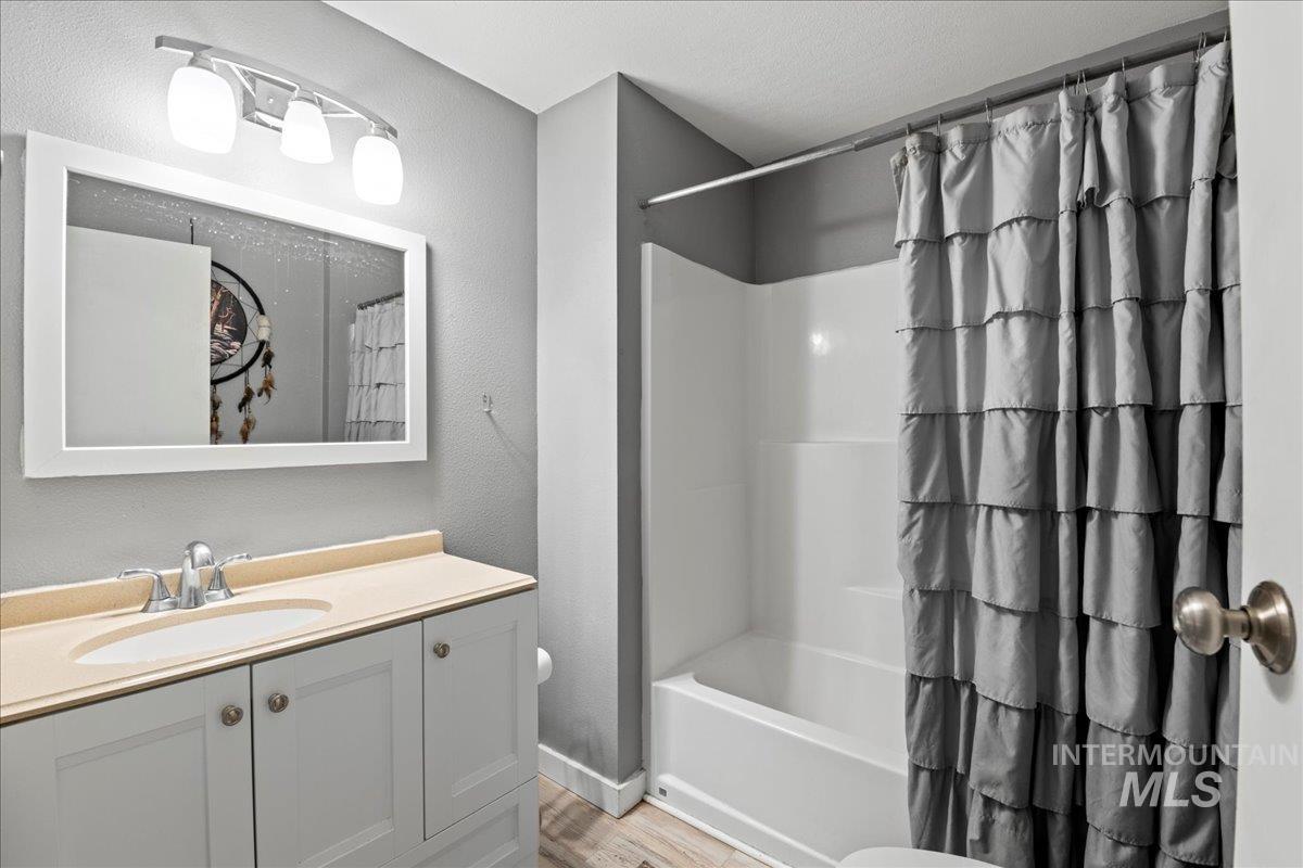 Bathroom with vanity, shower / bath combo with shower curtain, a textured wall, and light wood-type flooring