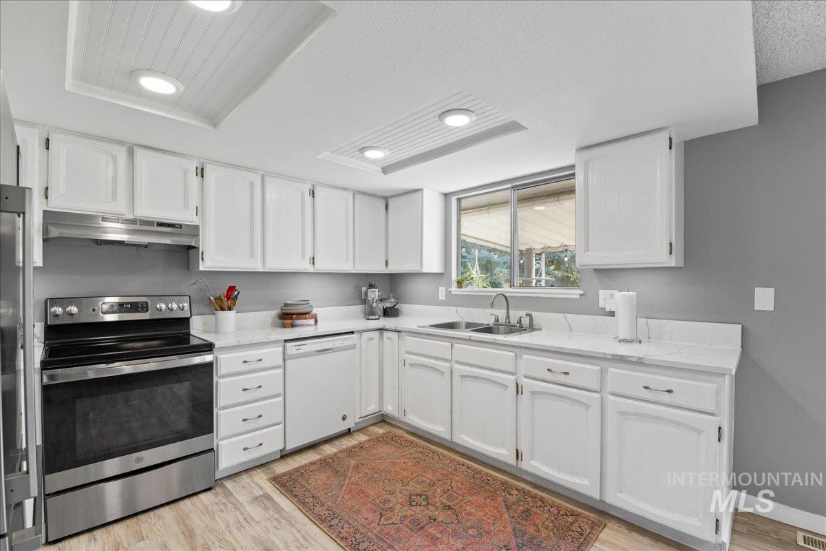 Kitchen featuring appliances with stainless steel finishes, white cabinets, light wood-style flooring, under cabinet range hood, and a textured ceiling