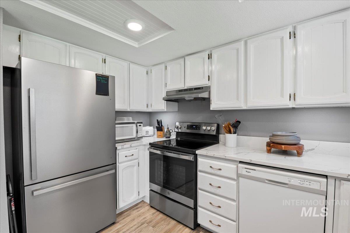 Kitchen with stainless steel appliances, white cabinetry, light wood-style floors, light stone counters, and recessed lighting