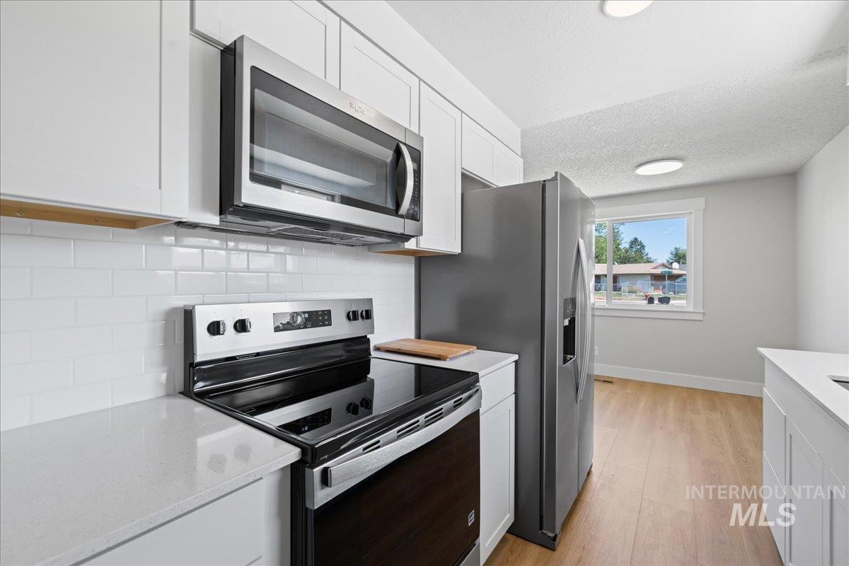 Kitchen with appliances with stainless steel finishes, tasteful backsplash, white cabinets, light wood-type flooring, and a textured ceiling