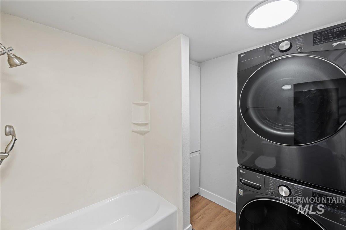 Laundry area featuring light wood-type flooring and stacked washing machine and dryer