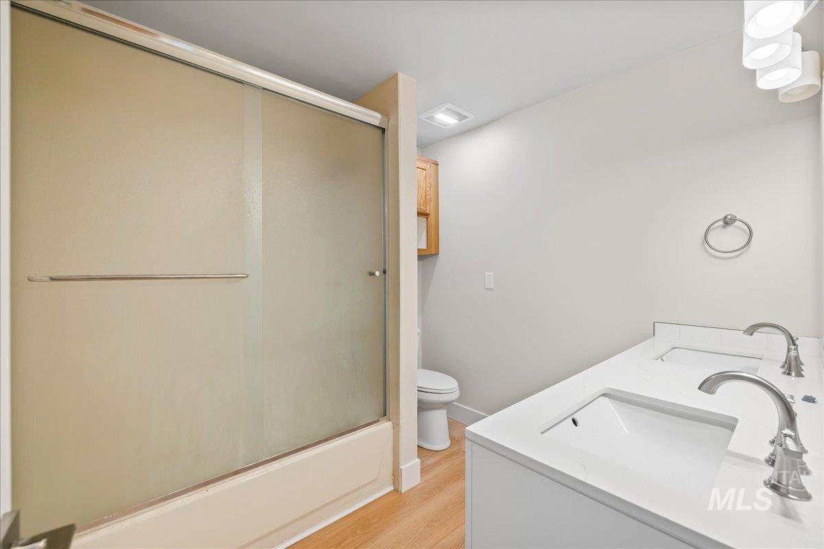 Bathroom featuring double vanity, light wood-type flooring, and shower / bath combination with glass door