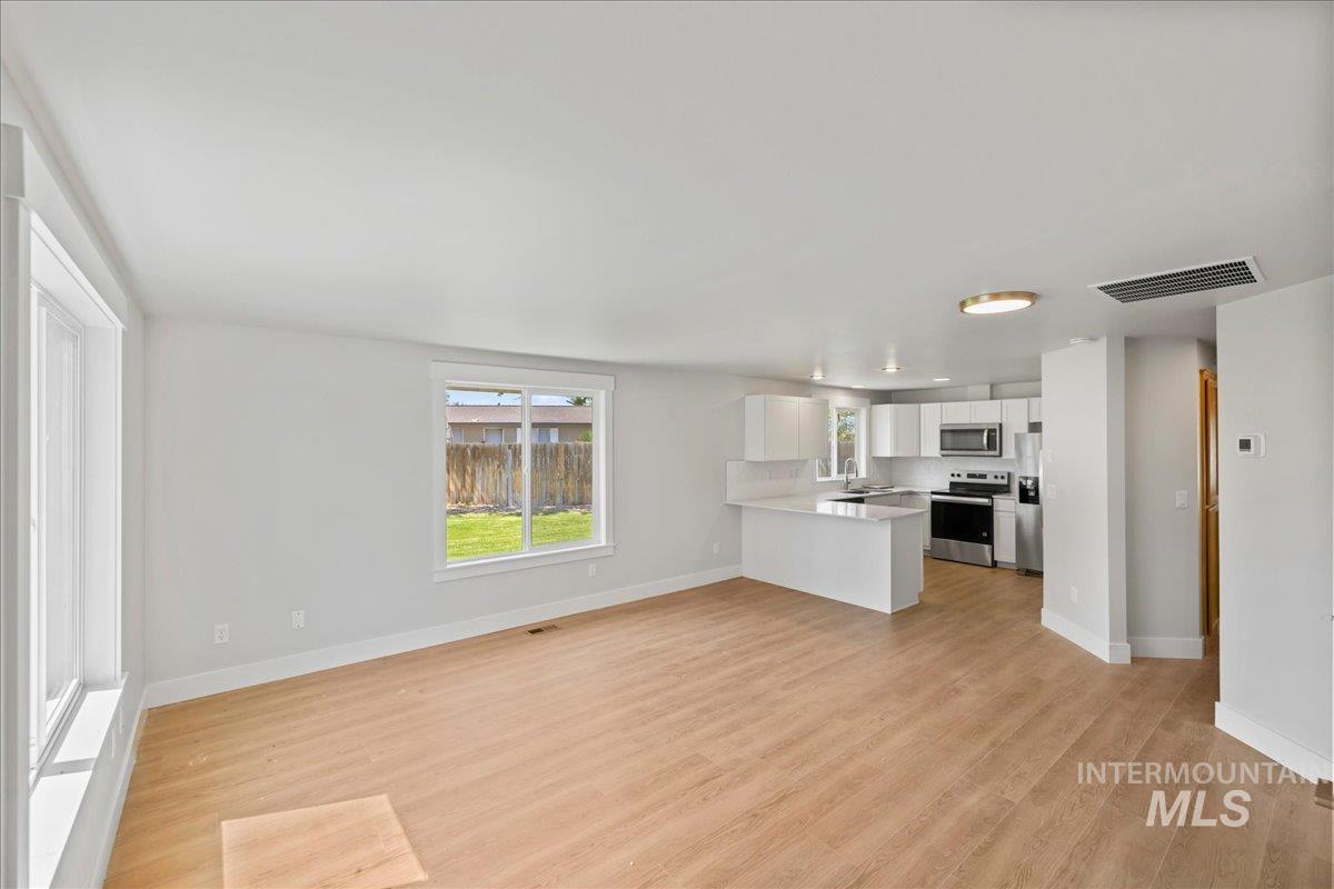 Kitchen featuring white cabinetry, appliances with stainless steel finishes, open floor plan, light wood-type flooring, and a peninsula