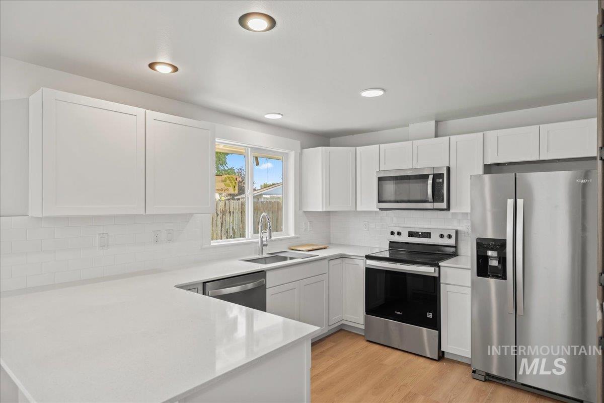 Kitchen with stainless steel appliances, light wood finished floors, white cabinets, a peninsula, and tasteful backsplash