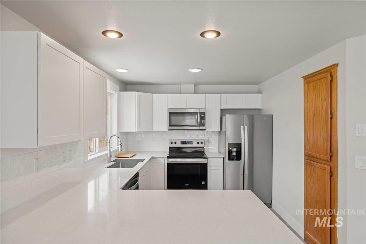 Kitchen featuring stainless steel appliances, white cabinets, tasteful backsplash, light stone countertops, and recessed lighting