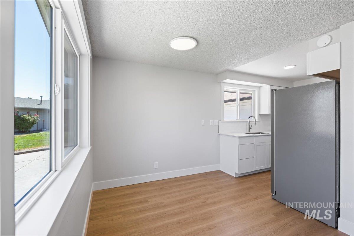 Kitchen with freestanding refrigerator, light countertops, white cabinets, light wood-style floors, and a textured ceiling