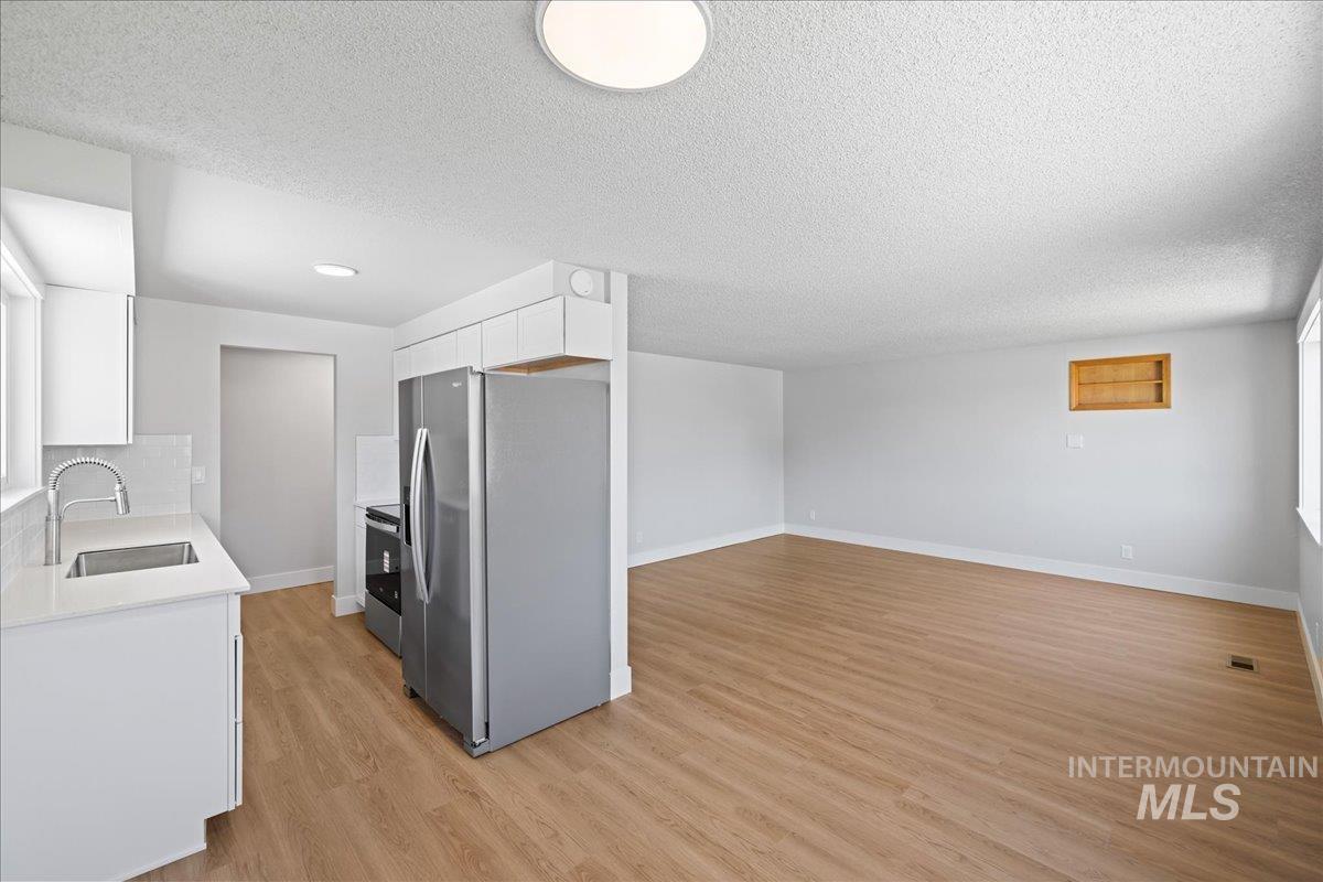 Kitchen featuring appliances with stainless steel finishes, white cabinetry, light wood-style flooring, a textured ceiling, and open floor plan