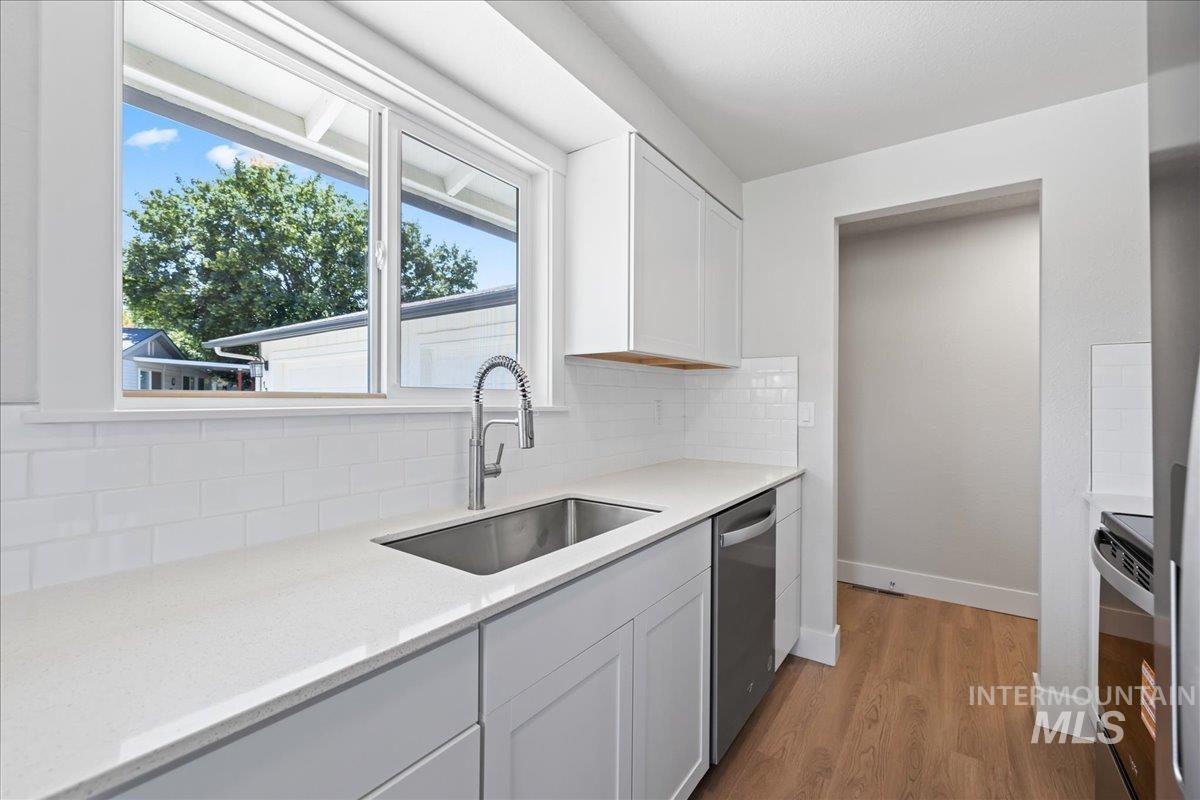 Kitchen with light wood-type flooring, white cabinetry, black electric range oven, and decorative backsplash