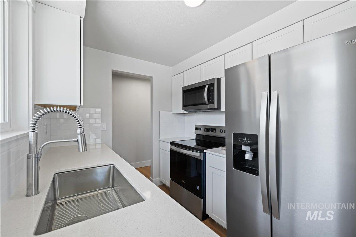 Kitchen featuring stainless steel appliances, white cabinets, tasteful backsplash, dark wood-style floors, and light stone counters