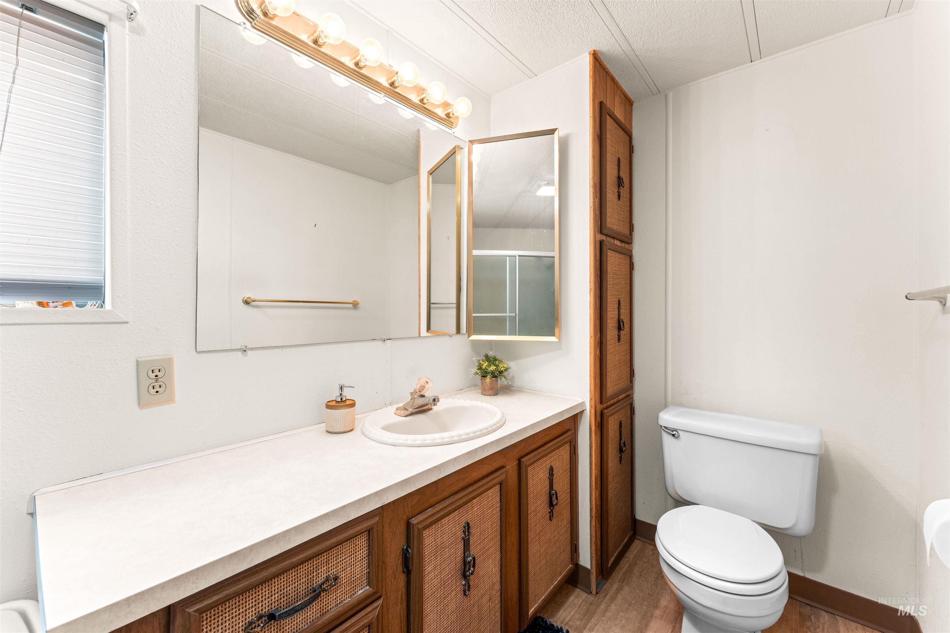 Bathroom with vanity, a shower with shower door, light wood finished floors, and a textured ceiling