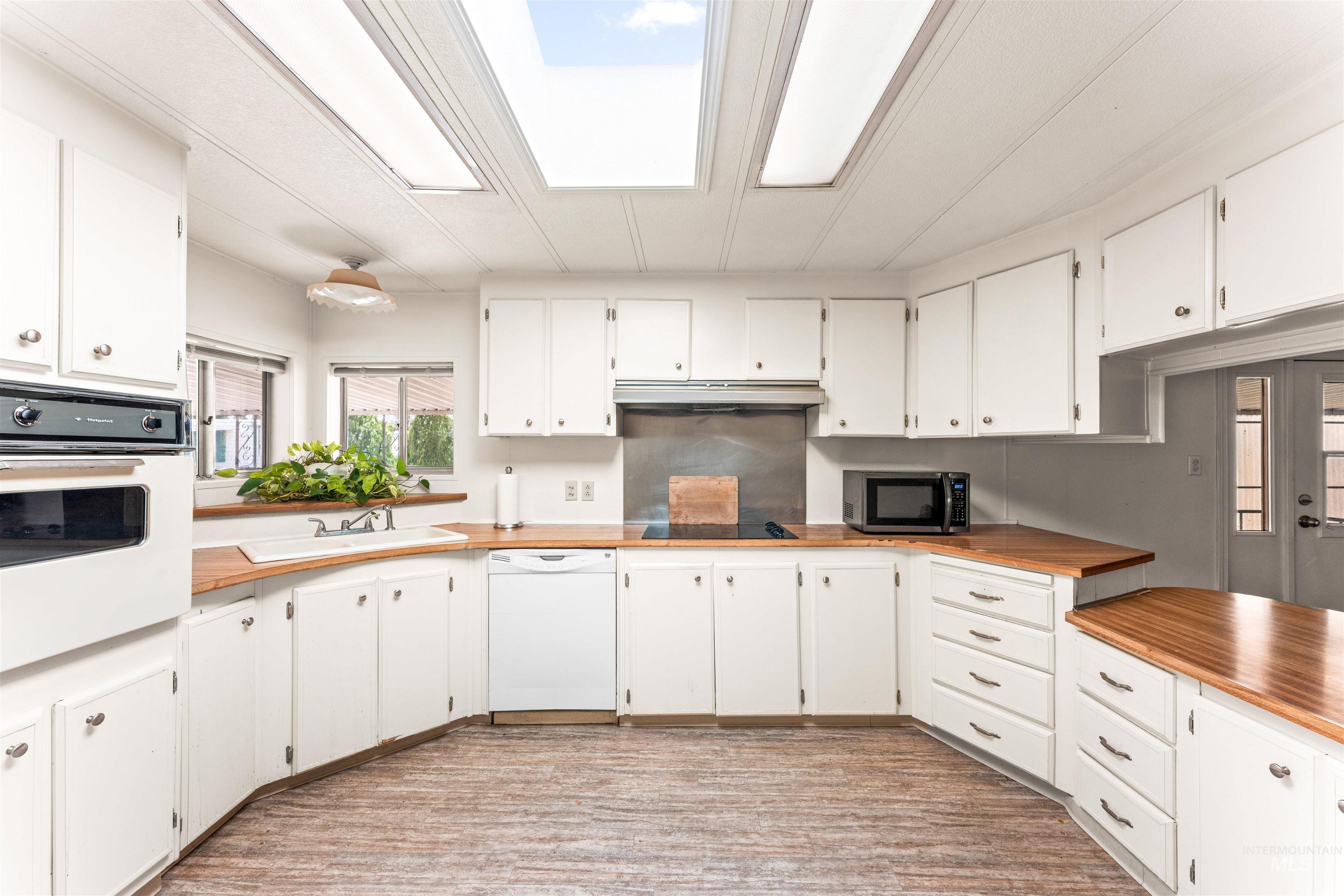 Kitchen featuring white cabinetry, white appliances, under cabinet range hood, and butcher block countertops