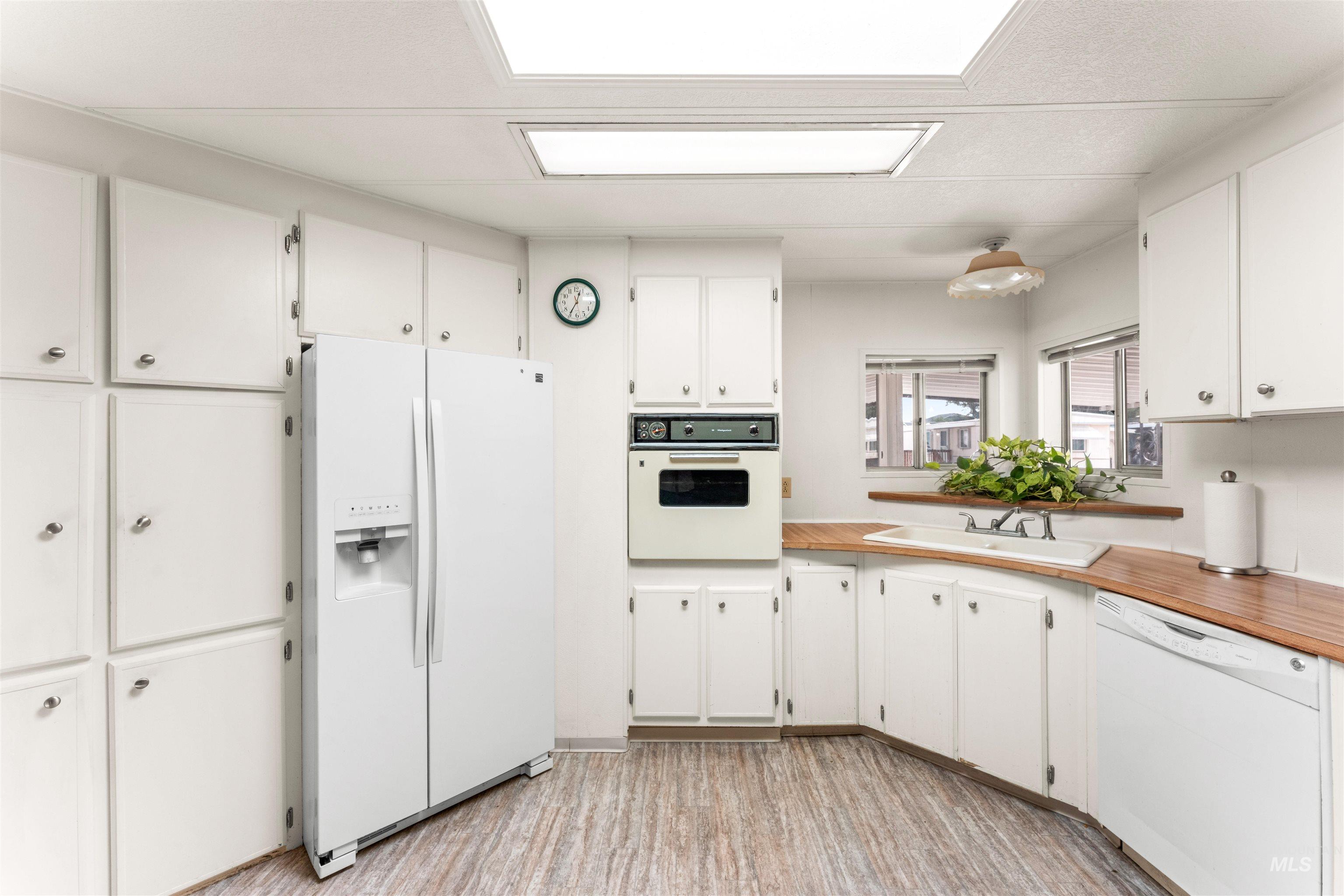 Kitchen featuring white appliances, white cabinetry, light wood-style flooring, and butcher block counters