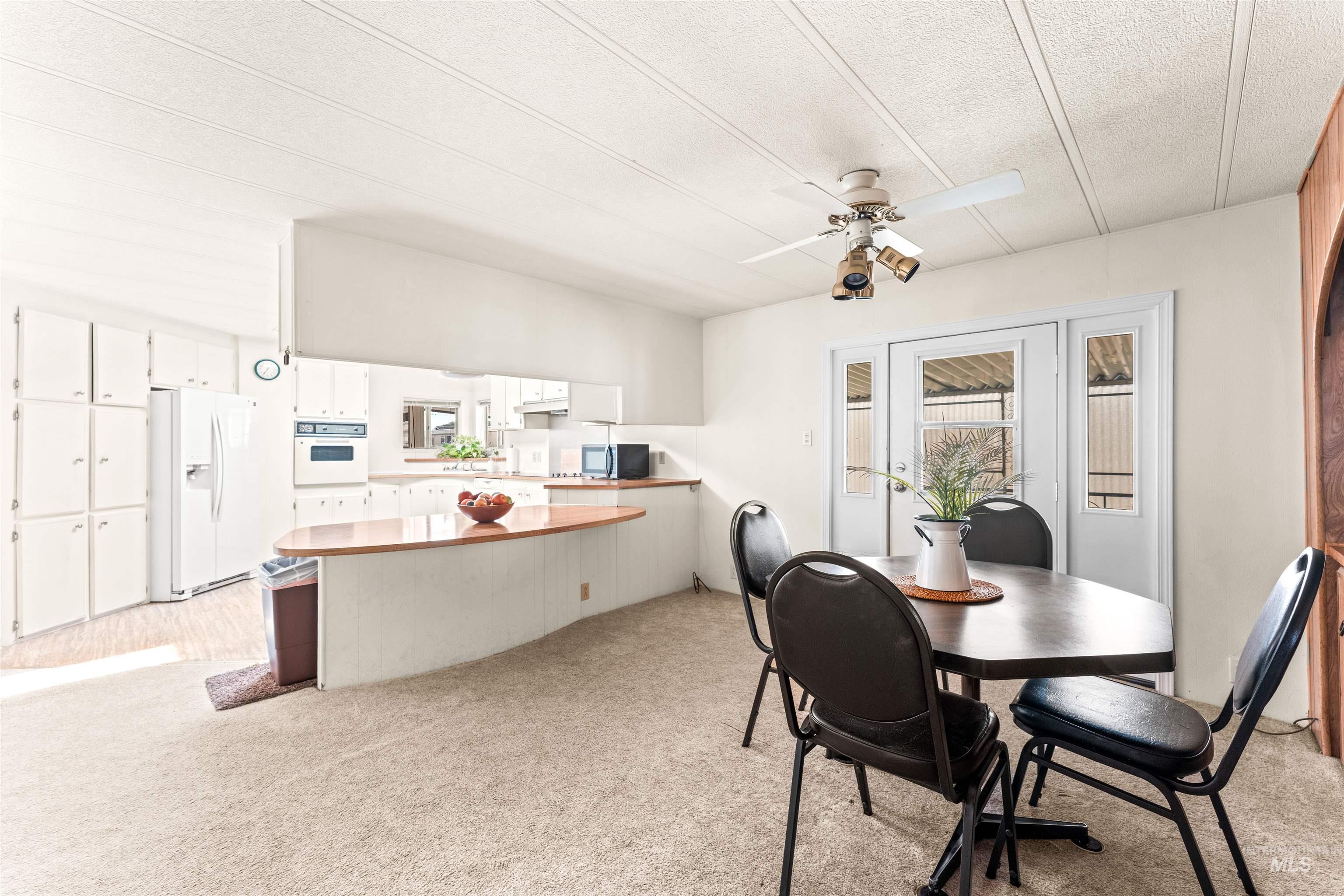 Dining space featuring a ceiling fan, light colored carpet, and a textured ceiling