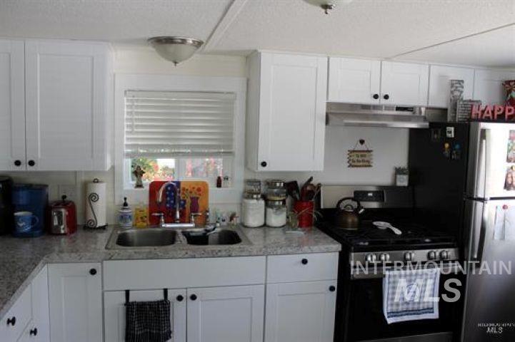 Kitchen with appliances with stainless steel finishes, white cabinetry, under cabinet range hood, a textured ceiling, and light stone counters
