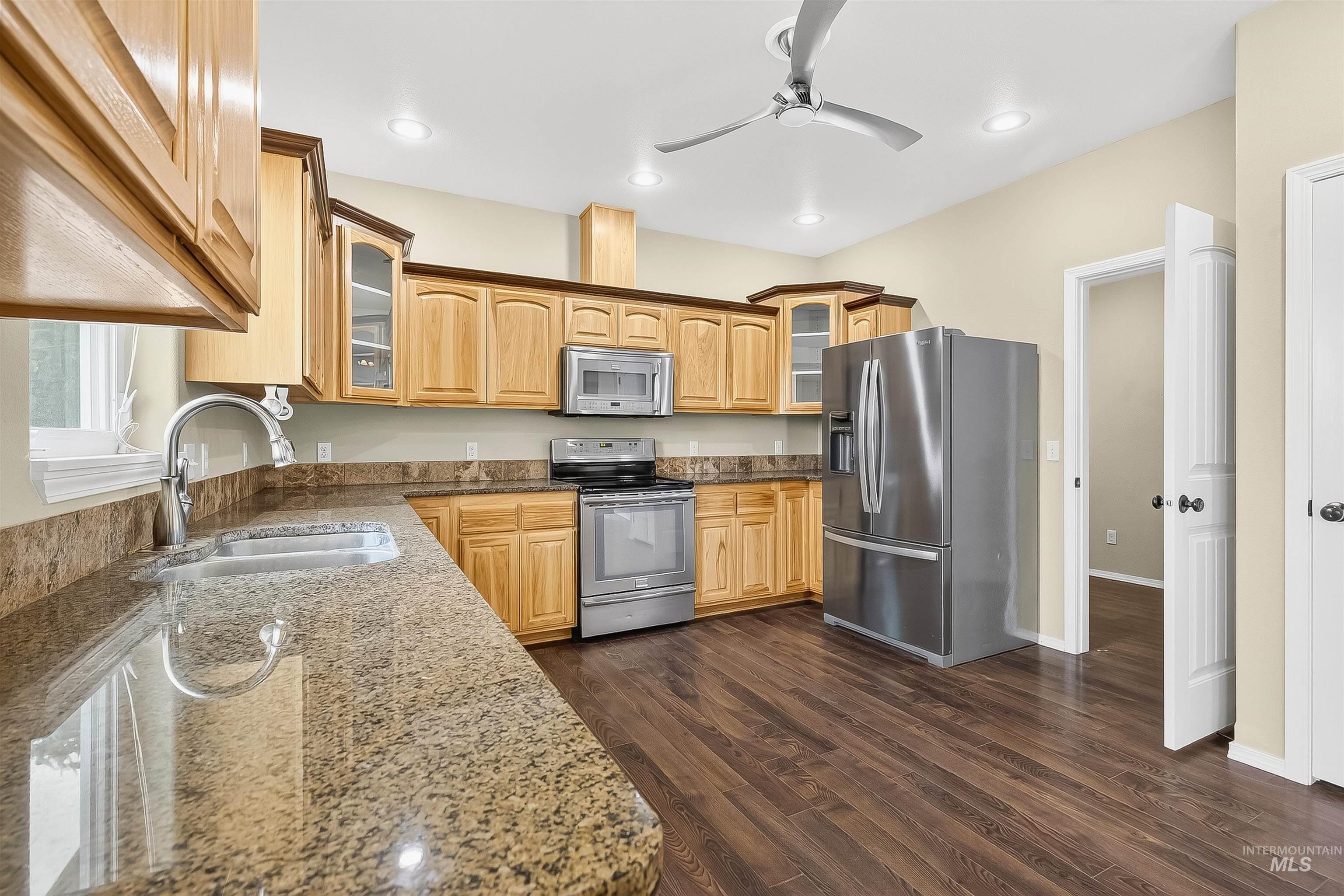 Kitchen featuring glass insert cabinets, appliances with stainless steel finishes, dark stone counters, dark wood finished floors, and recessed lighting