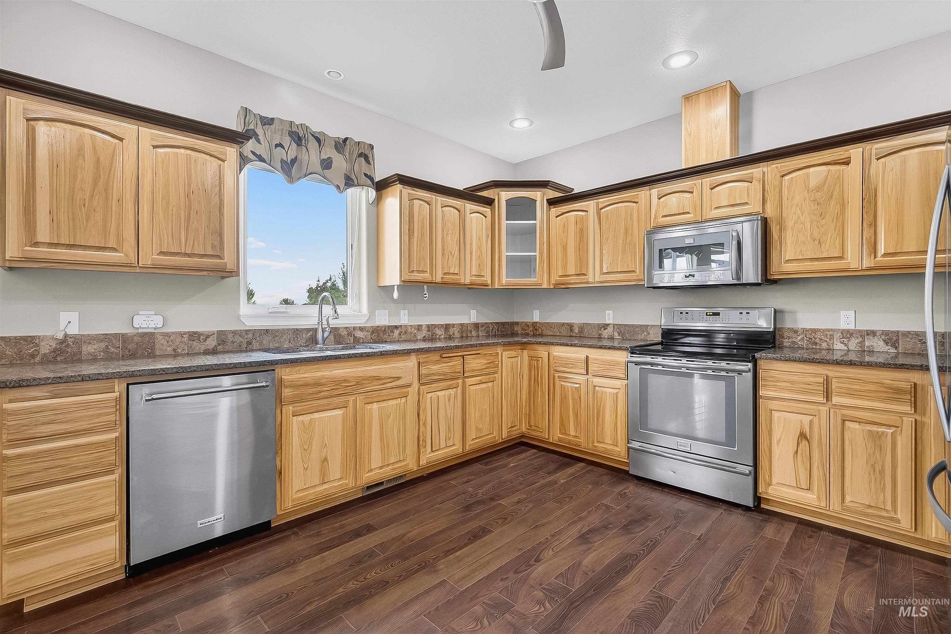 Kitchen with stainless steel appliances, dark wood-type flooring, dark stone countertops, glass insert cabinets, and recessed lighting