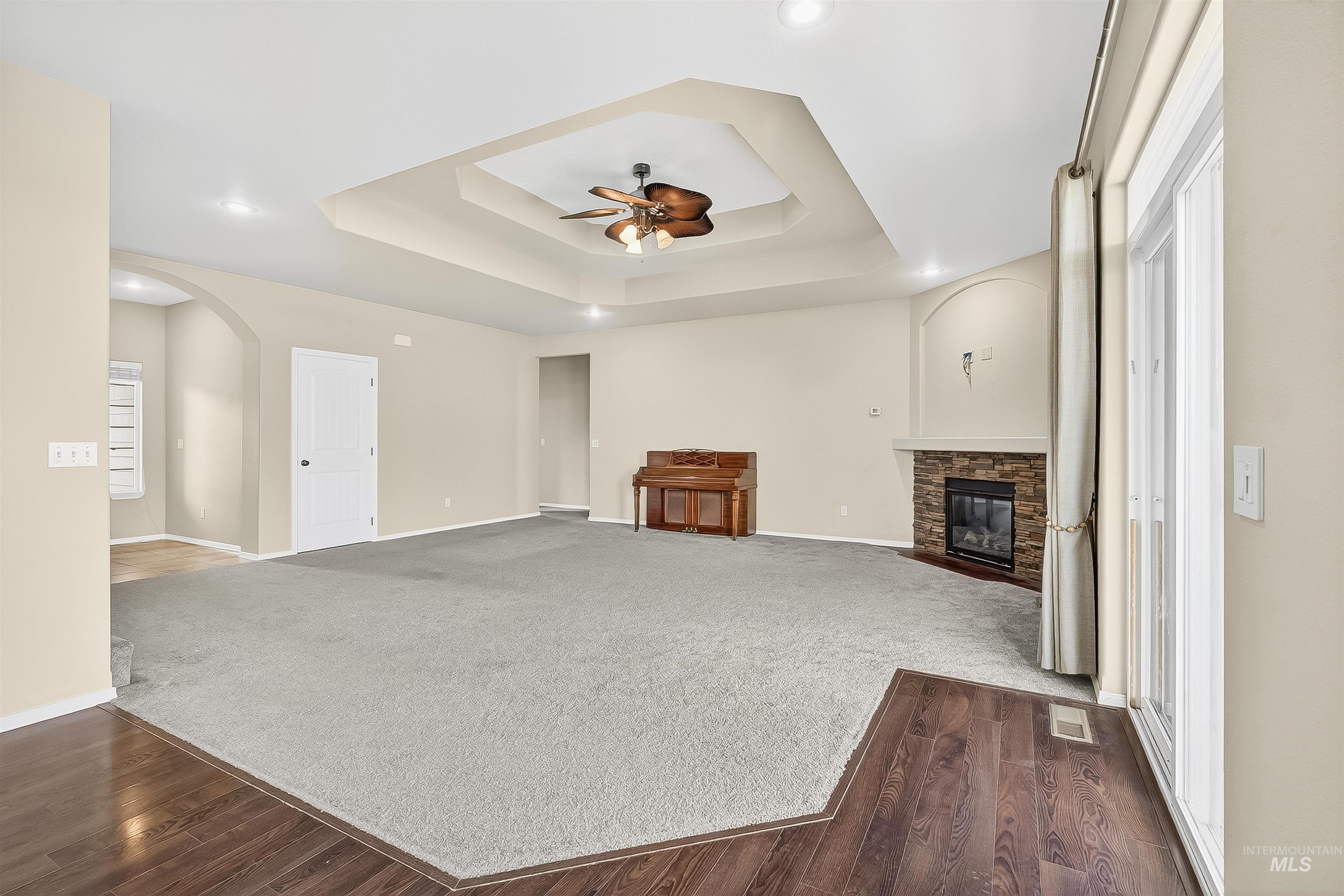 Unfurnished living room featuring dark wood-style flooring, a fireplace, a tray ceiling, and dark carpet