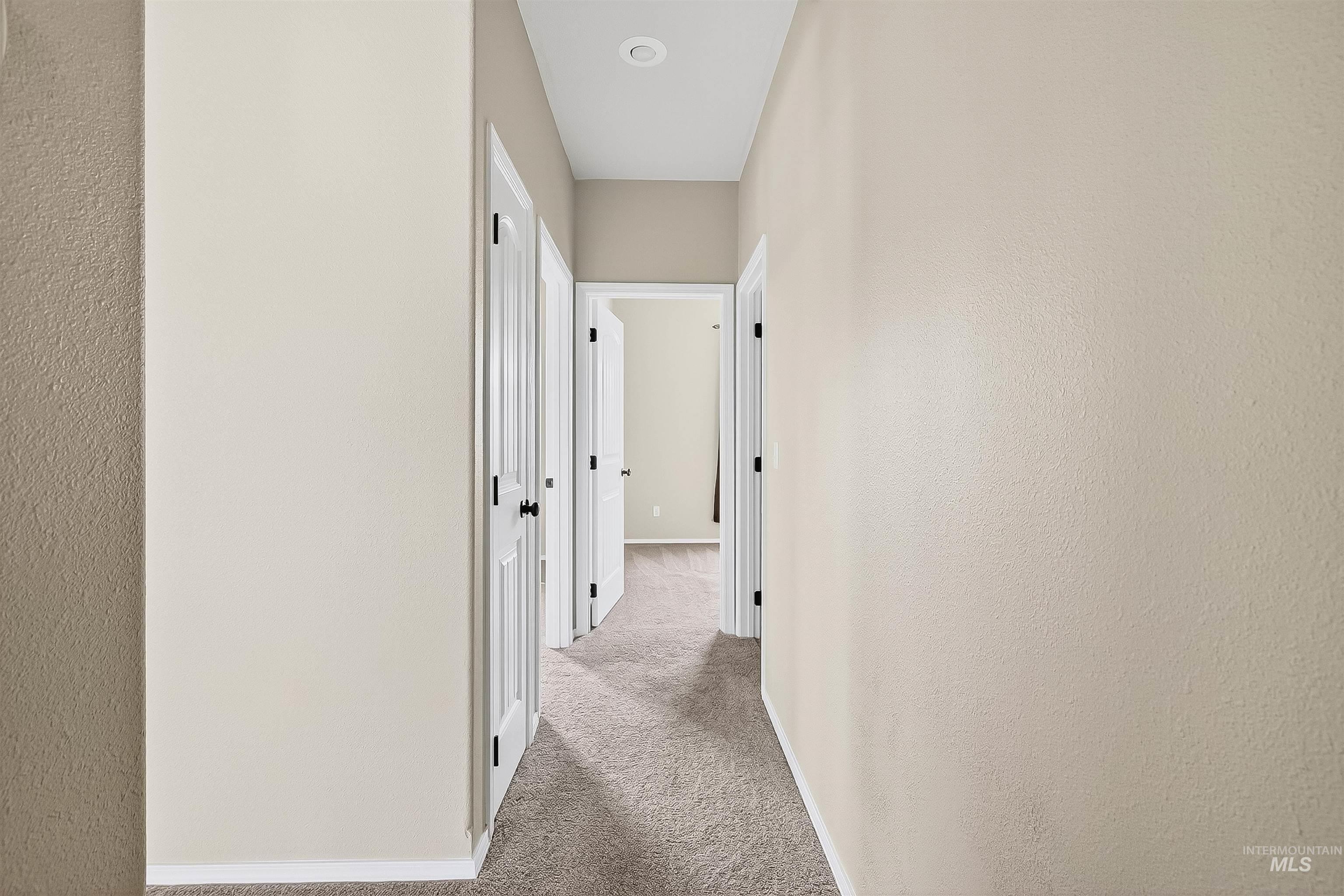 Hallway featuring light colored carpet and a textured wall
