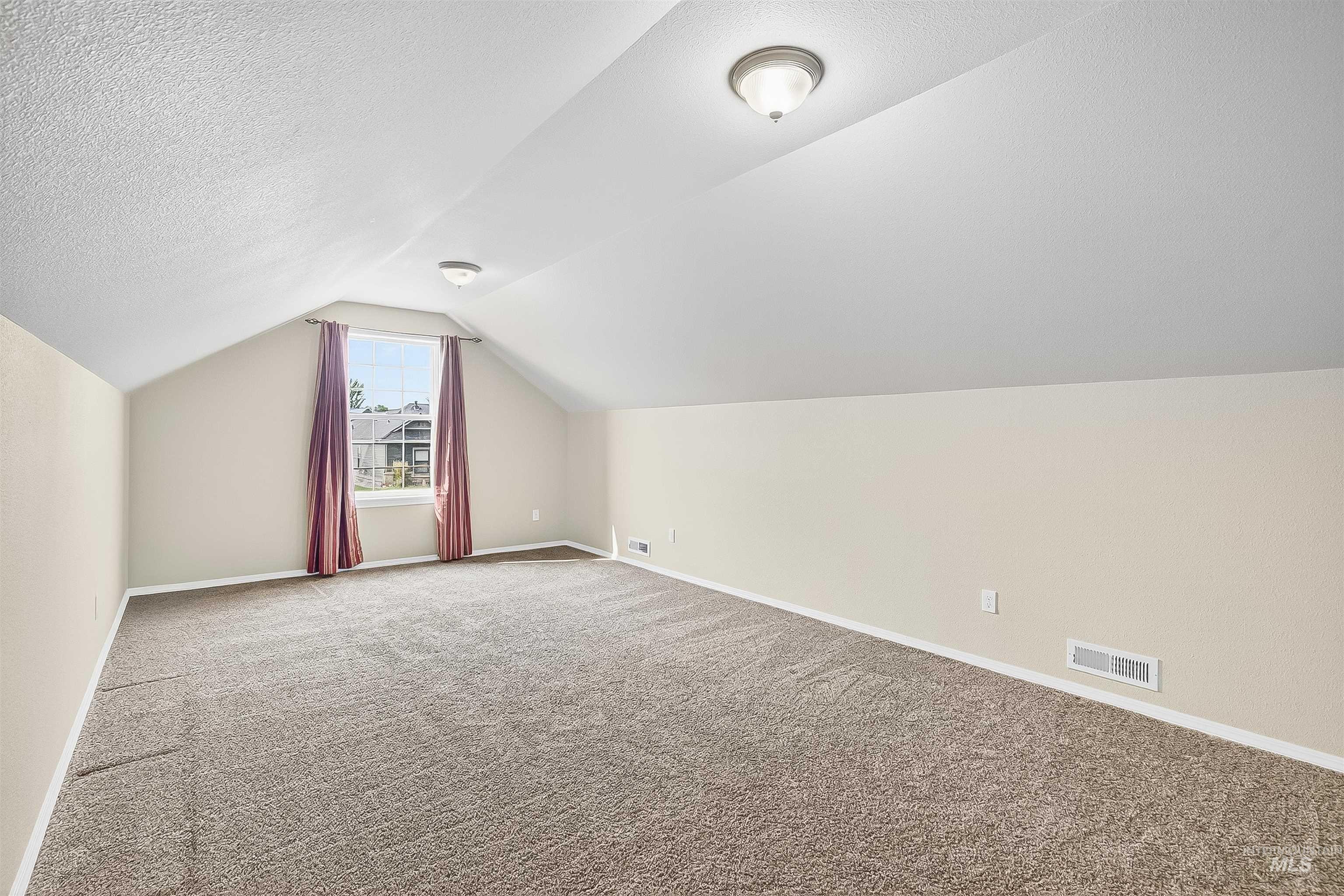 Additional living space featuring light carpet, vaulted ceiling, and a textured ceiling