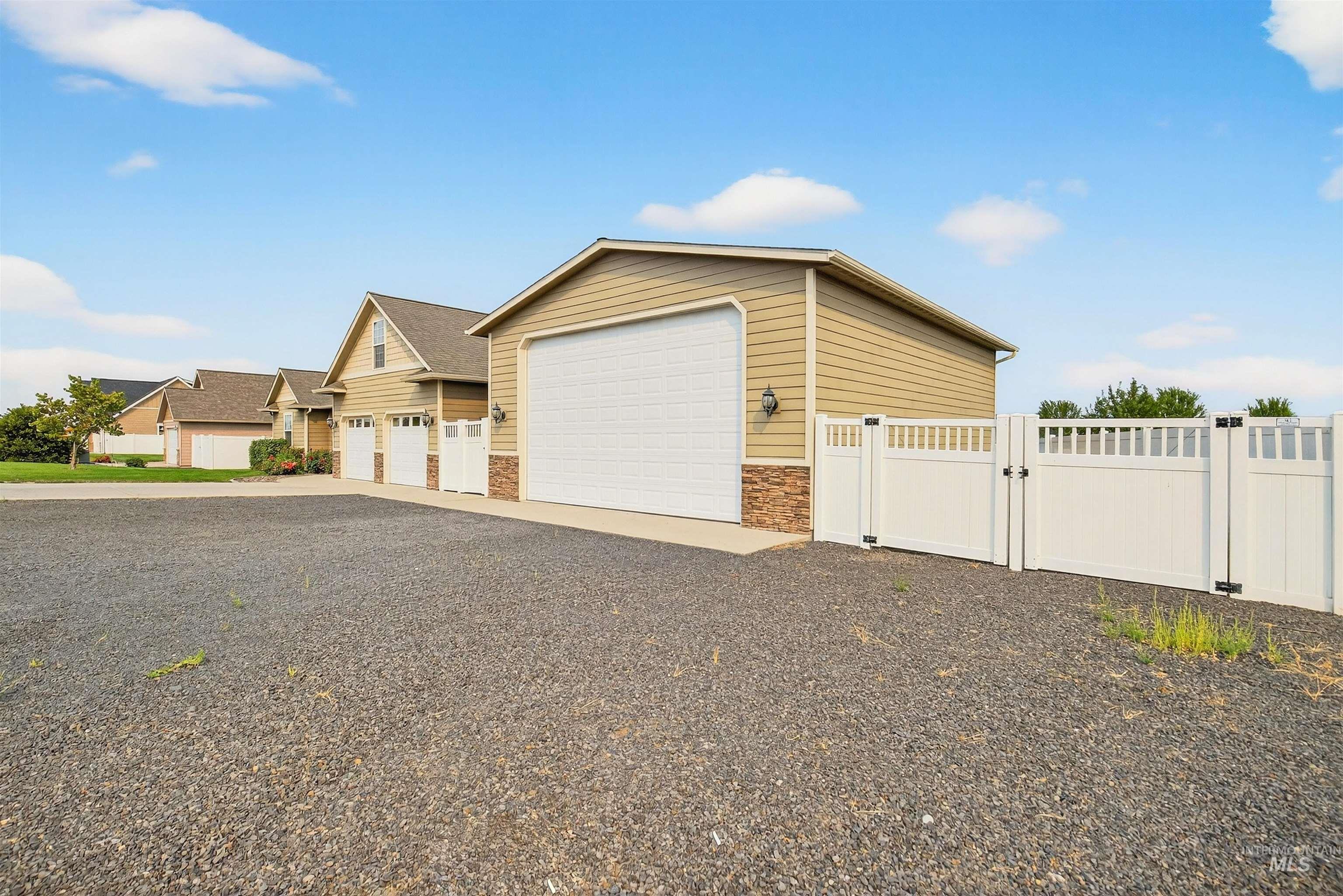 View of front of home with a gate, stone siding, an outbuilding, driveway, and a garage