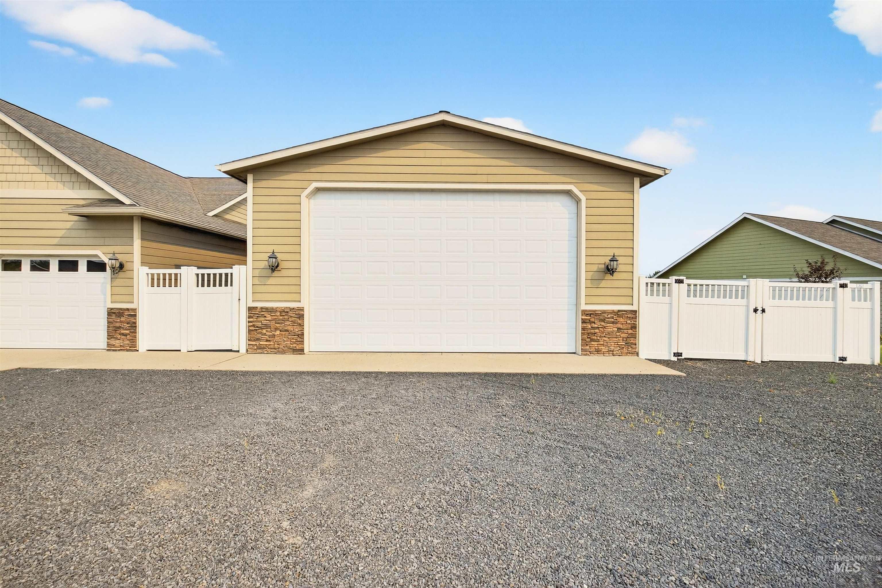 View of front facade with stone siding, a garage, a gate, and an outbuilding