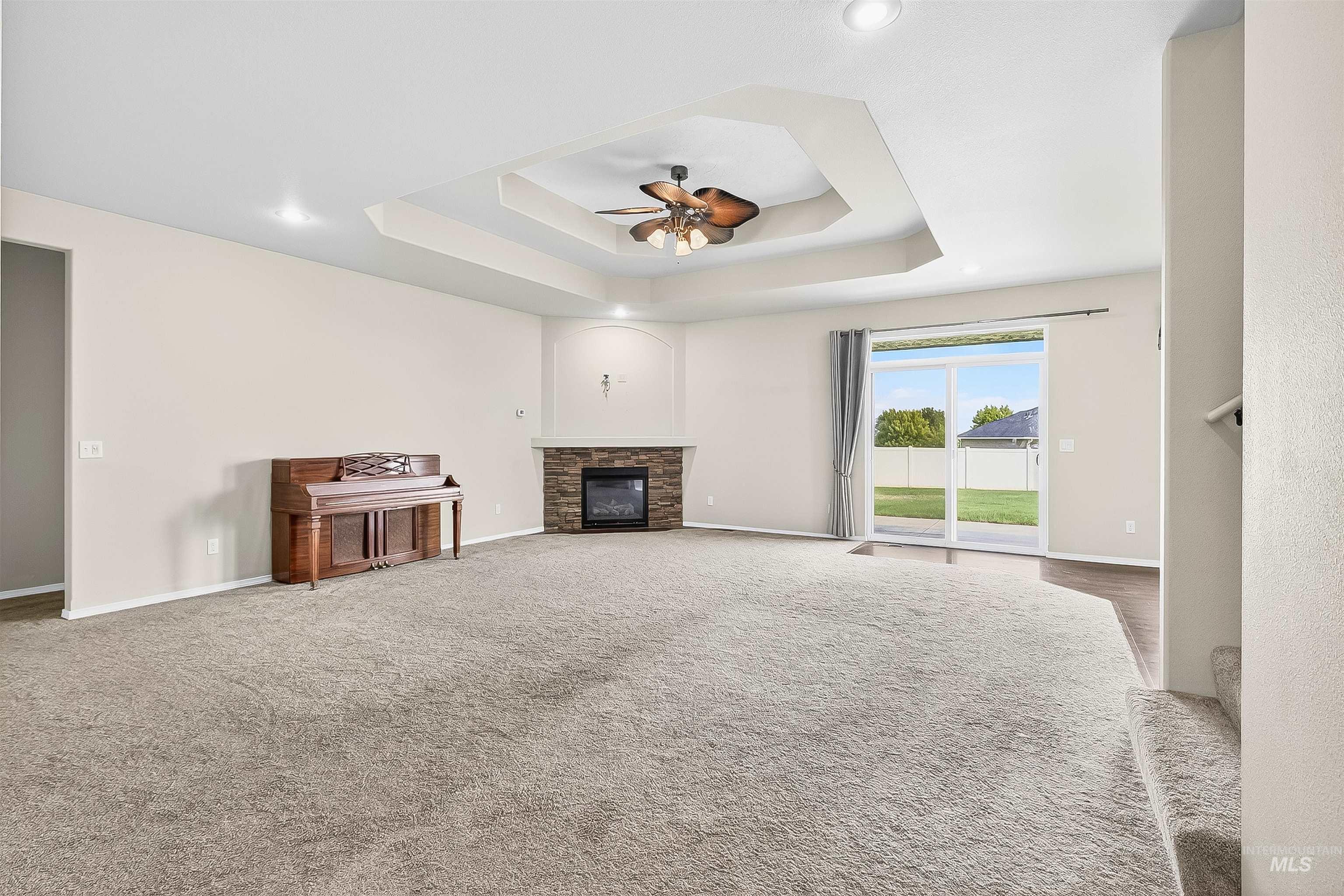Unfurnished living room featuring a stone fireplace, ceiling fan, a raised ceiling, and carpet floors