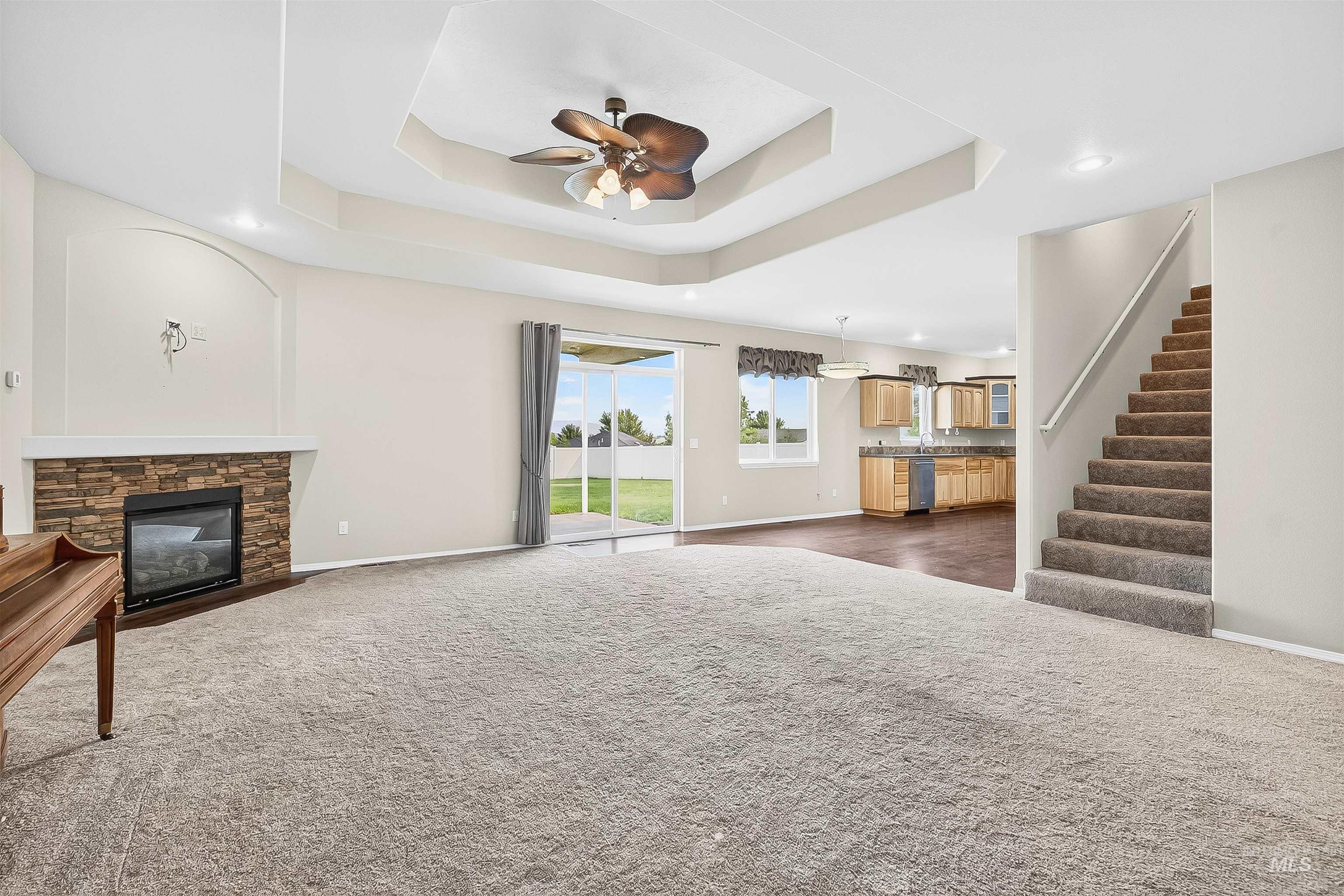 Unfurnished living room featuring a stone fireplace, stairs, dark colored carpet, a ceiling fan, and recessed lighting