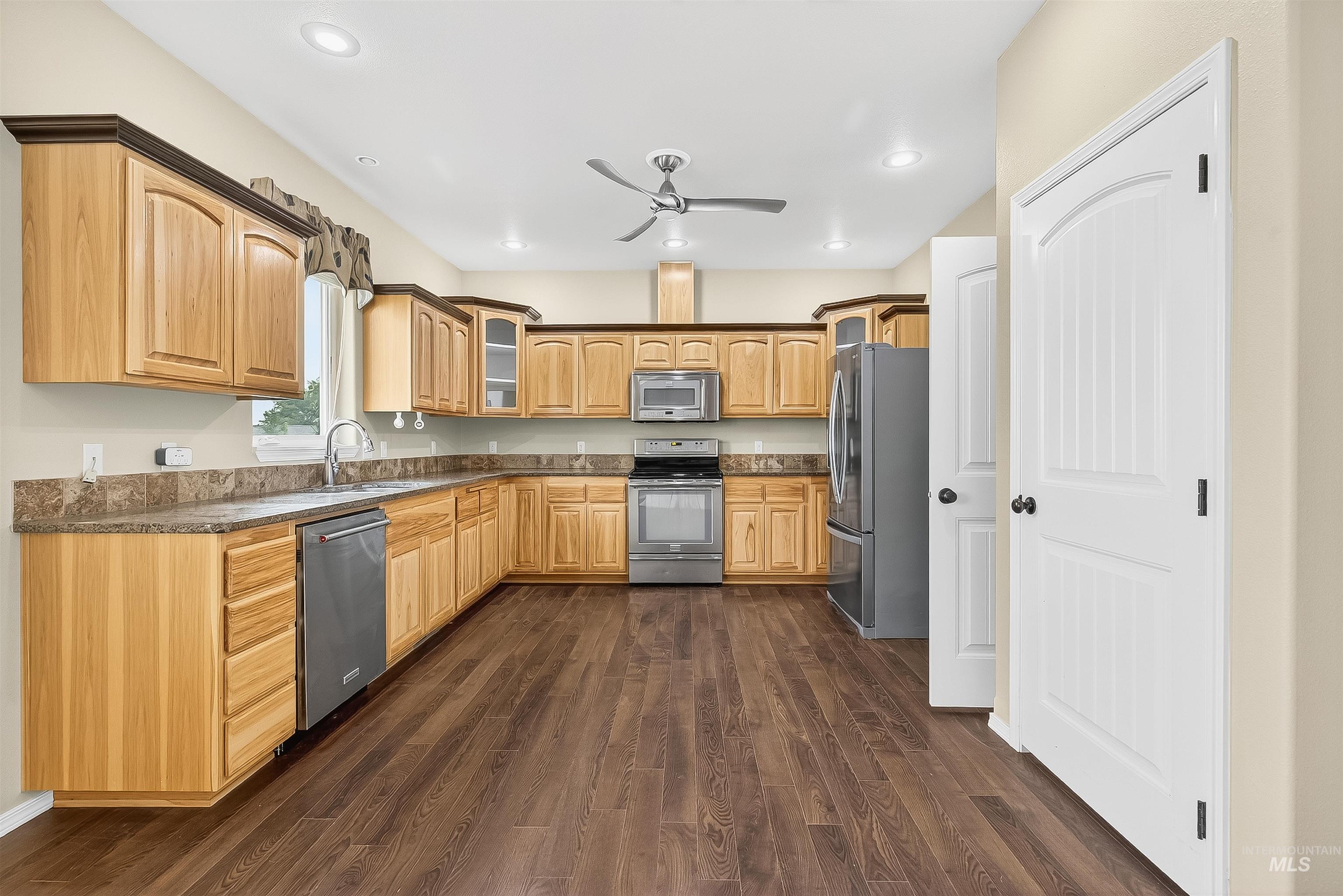 Kitchen featuring glass insert cabinets, dark wood-style flooring, stainless steel appliances, ceiling fan, and recessed lighting