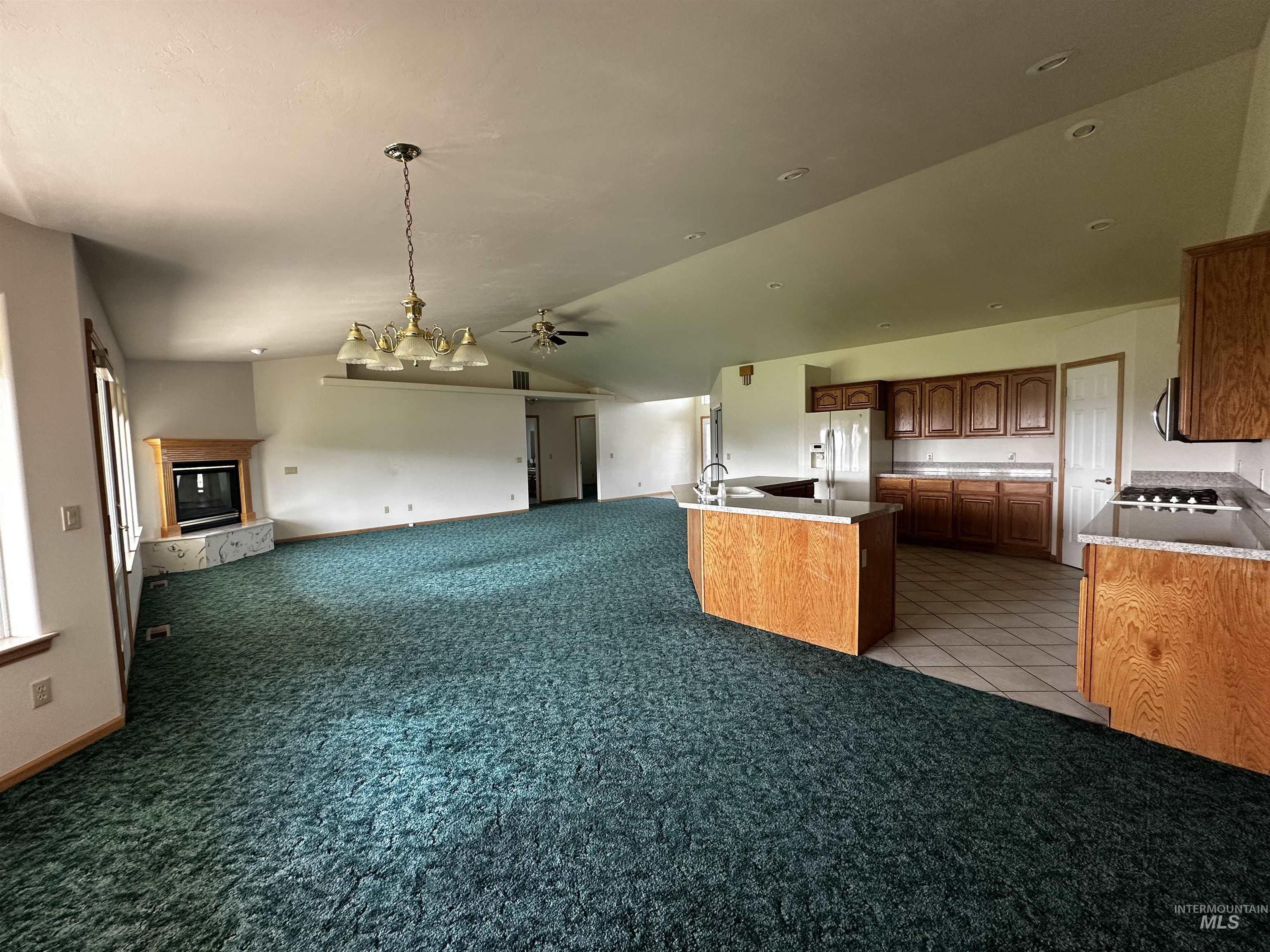 Kitchen featuring vaulted ceiling, open floor plan, light carpet, fridge with ice dispenser, and pendant lighting